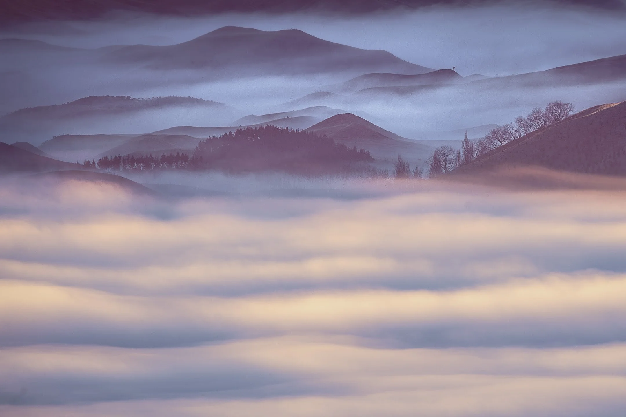 Bands of fog drift through the Tukituki Valley at sunrise, their tips catching the first warm light while distant hills remain in deep shadow, Hawke's Bay, New Zealand