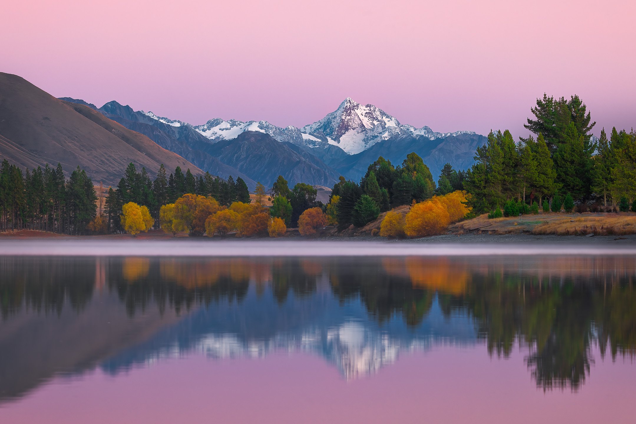 Mount D'Archaic reflected in the still dawn surface of Lake Camp, its snow-covered peaks doubled in the calm water moments before the wind arrived, Ashburton Lakes, Canterbury, New Zealand.