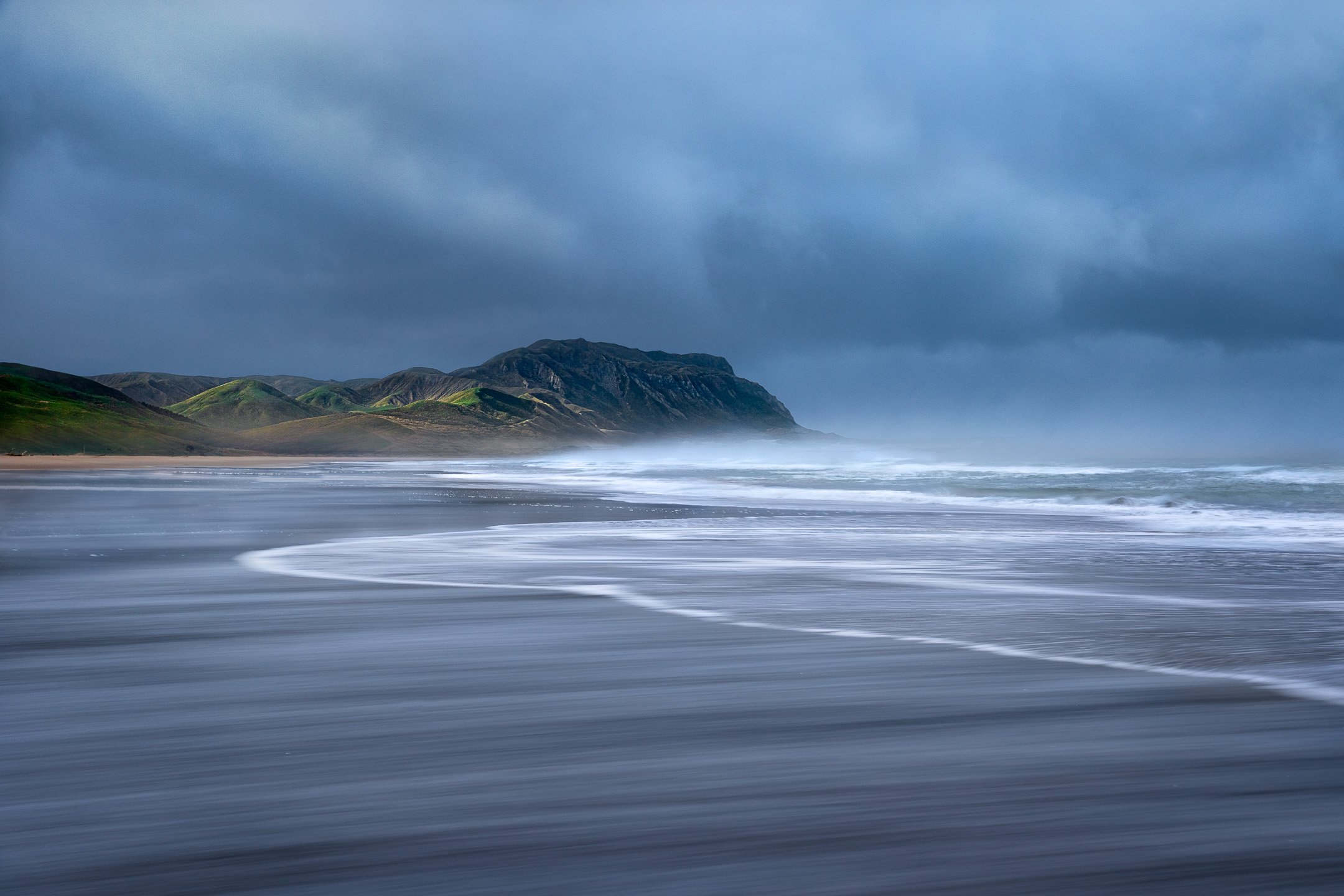 Long exposure of storm clouds gathering over reflective sand flats at Herbertville Beach, Cape Turnagain, New Zealand