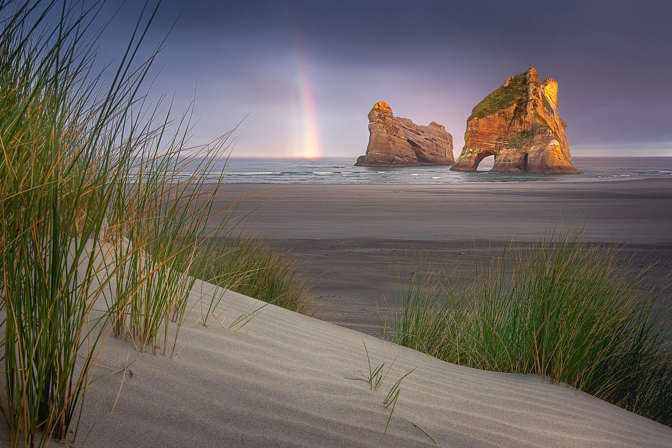 Rainbow arcing over the Archway Islands sea stacks at sunrise, Wharariki Beach, Tasman, New Zealand