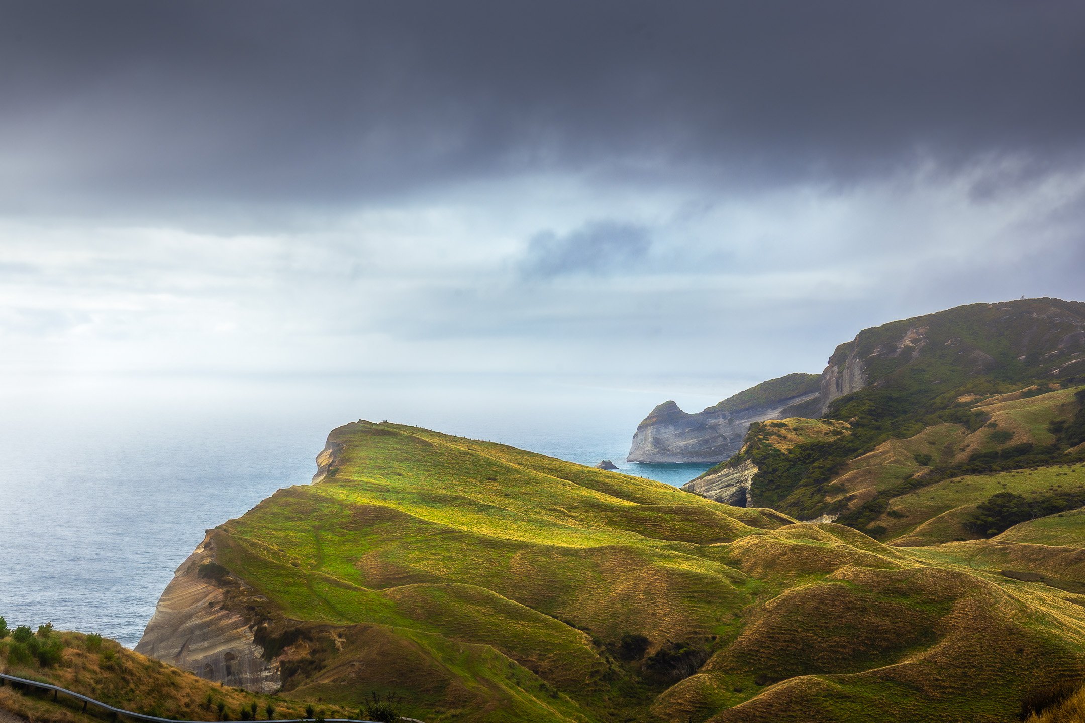 Shaft of storm light breaking over green cliffs at Pillar Point, Puponga Hilltop Walk, Tasman, New Zealand