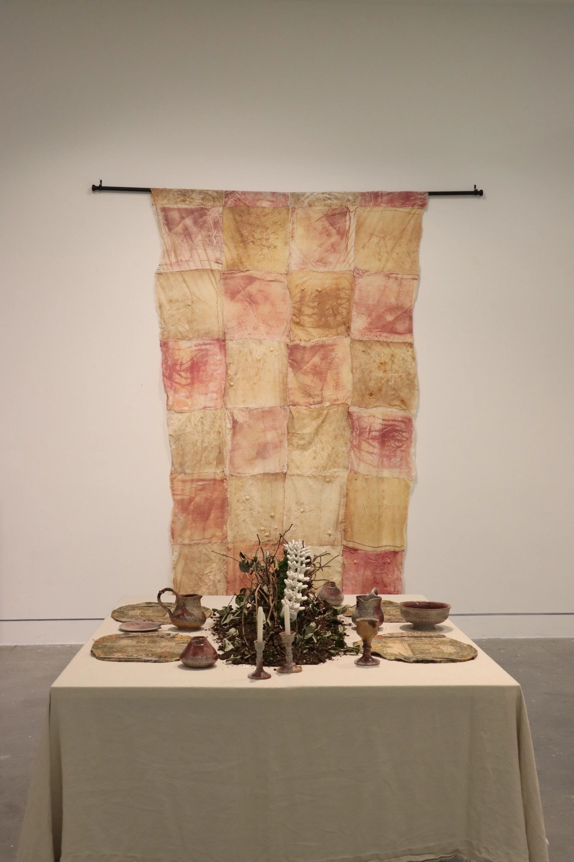 Dining Table: head on view. 
Pi Kuptasthien, "DERMIS PLAID: Wall Quilt", textiles, latex, cotton balls, paint, screen printing, approx. 118 x 79 x 10". 