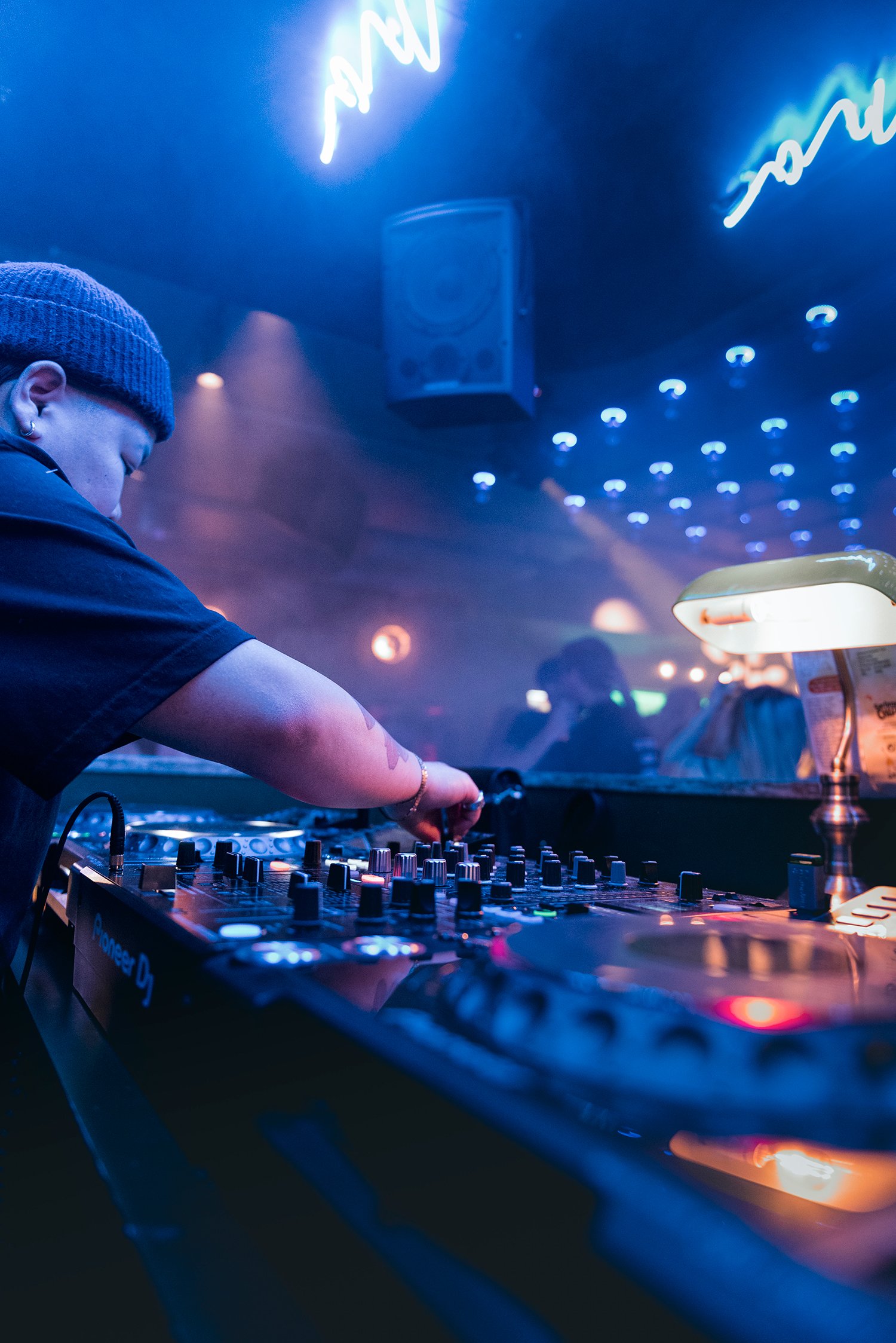 En DJ som justerer på miksebordet med dansegulvet i bakgrunnen