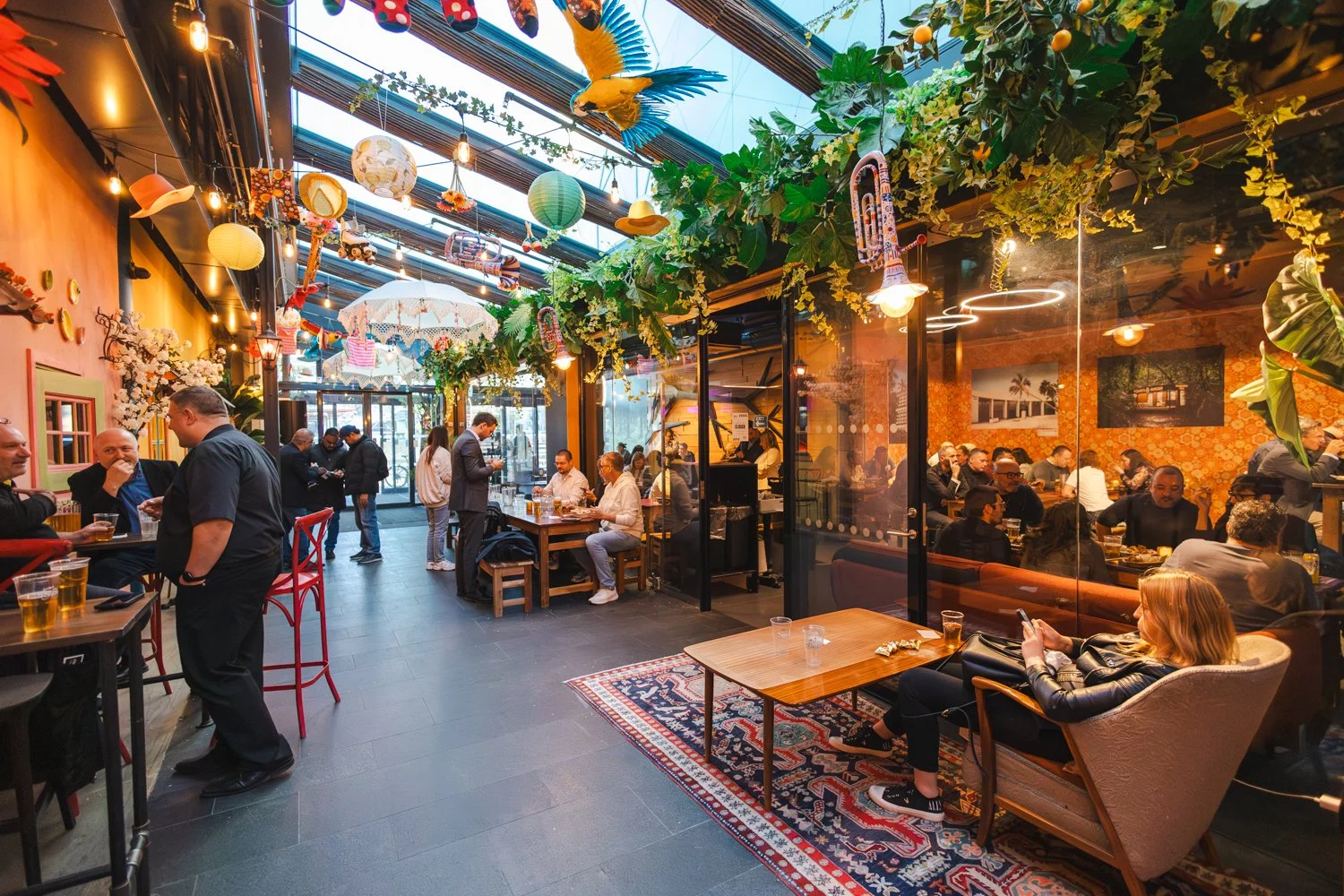 Selskapslokaler med elementer hengende fra taket og mennesker som sitter og spiser i ulike sittegrupper hos Barcode Street Food