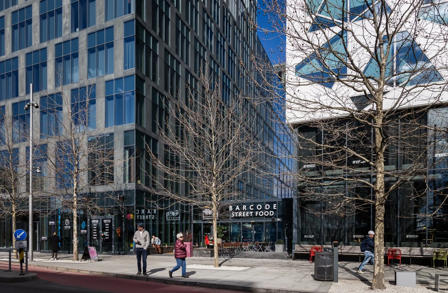 Utenfor inngangen til Barcode Street Food, mennesker går forbi og sola skinner.