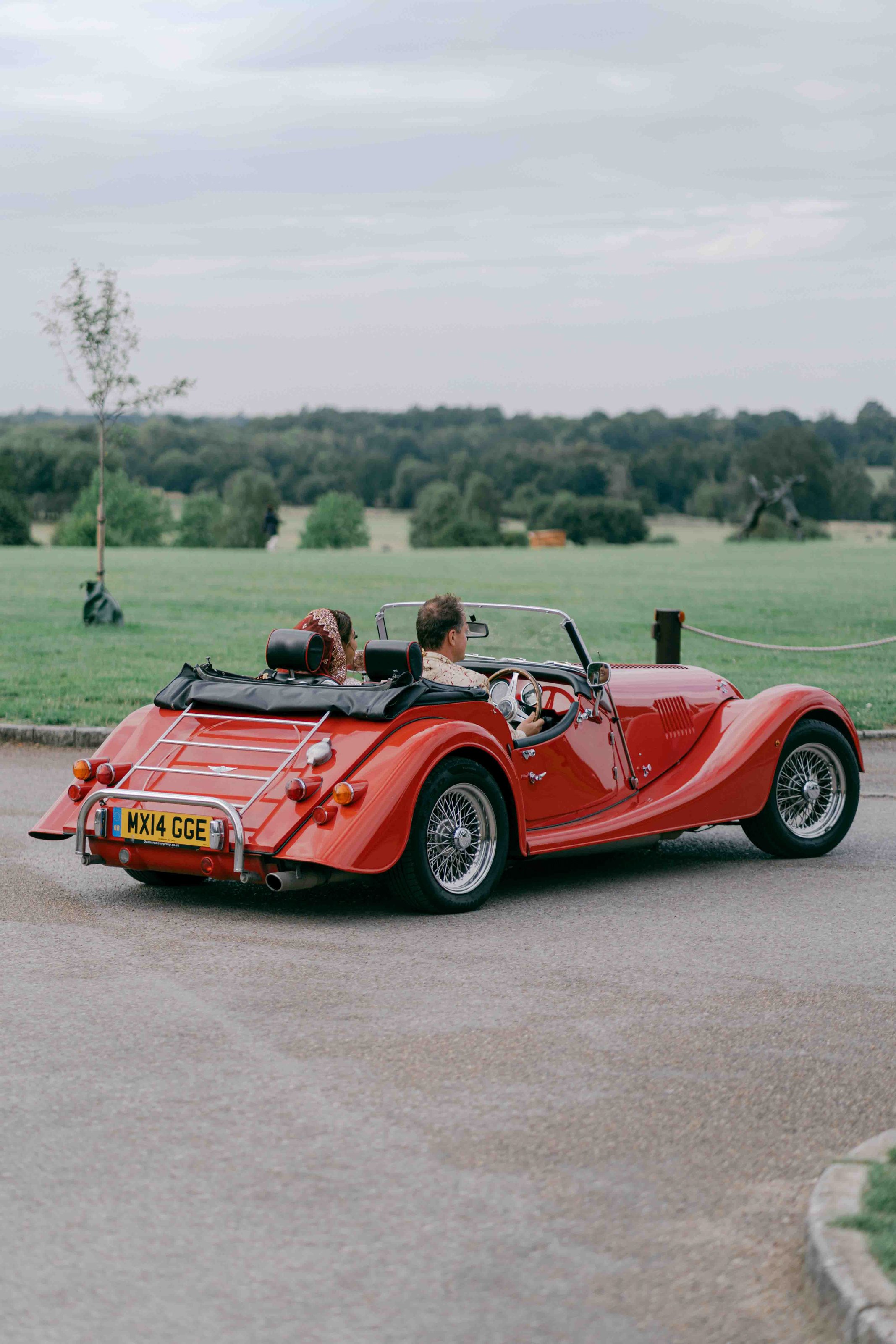  bride and groom driving off in a red classic car 