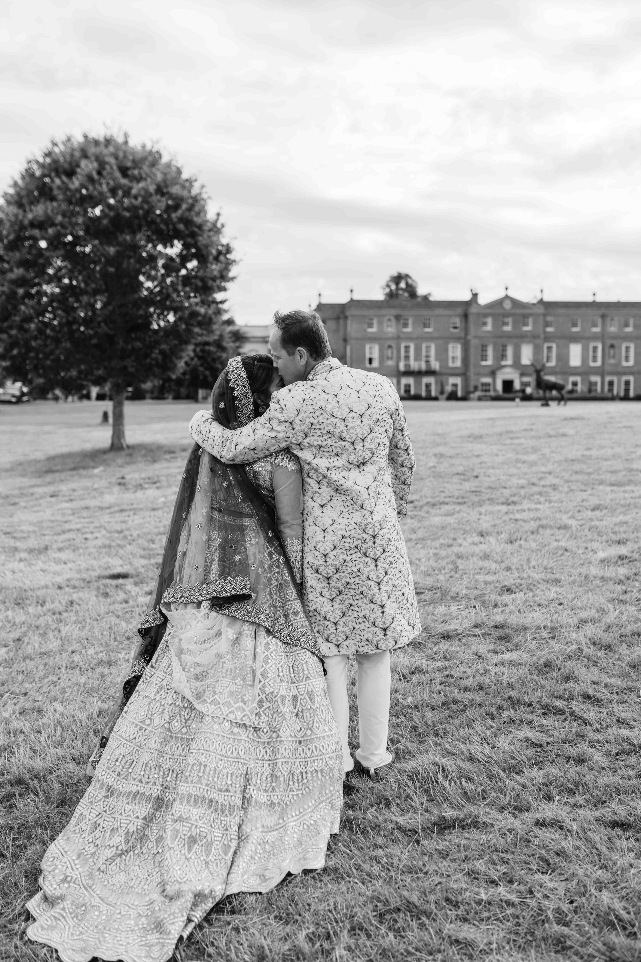  black and white photo of groom kissing bride’s head walking towards the four seasons hampshire 