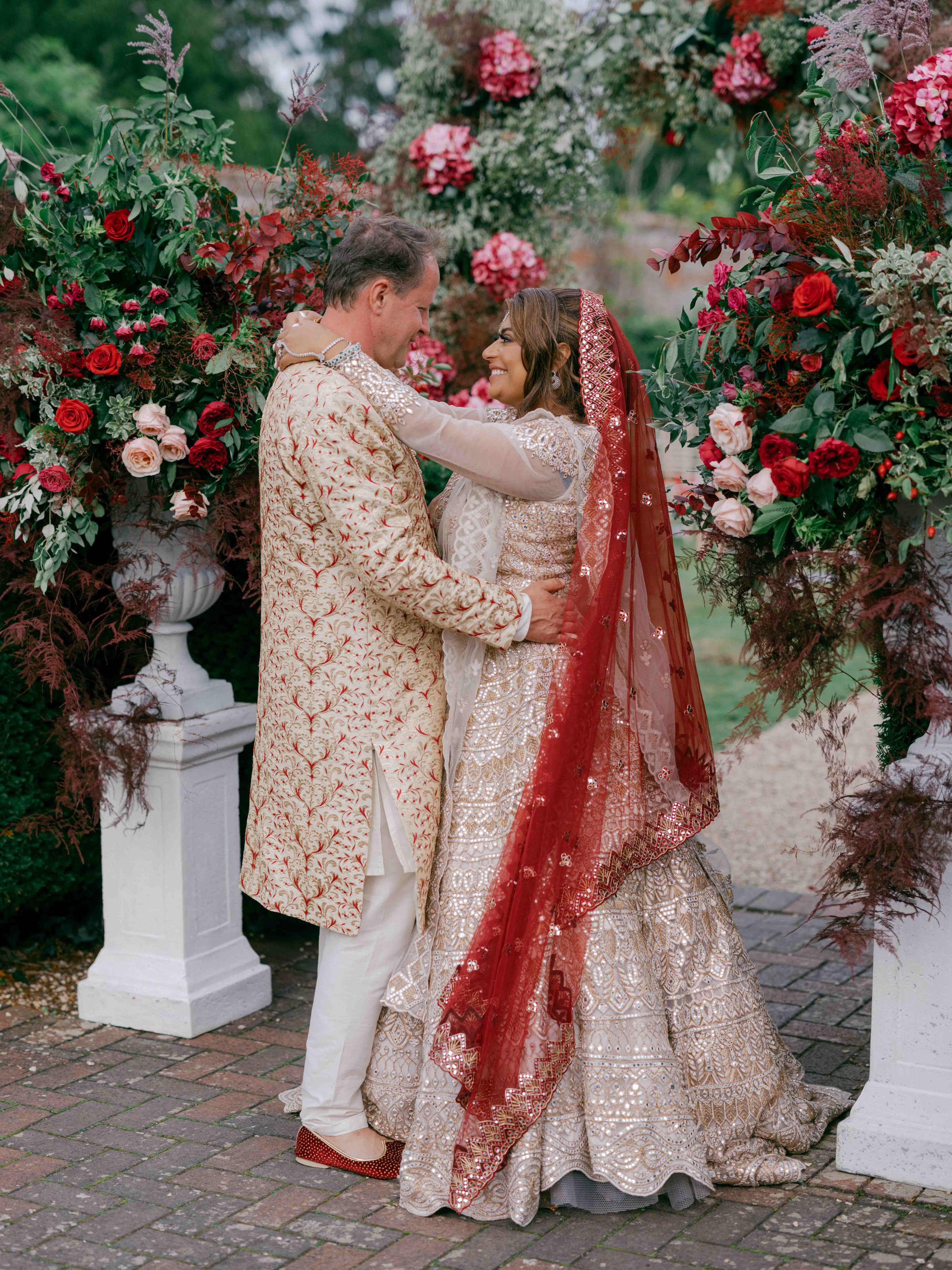  bride and groom hugging each other underneath a floral arch 