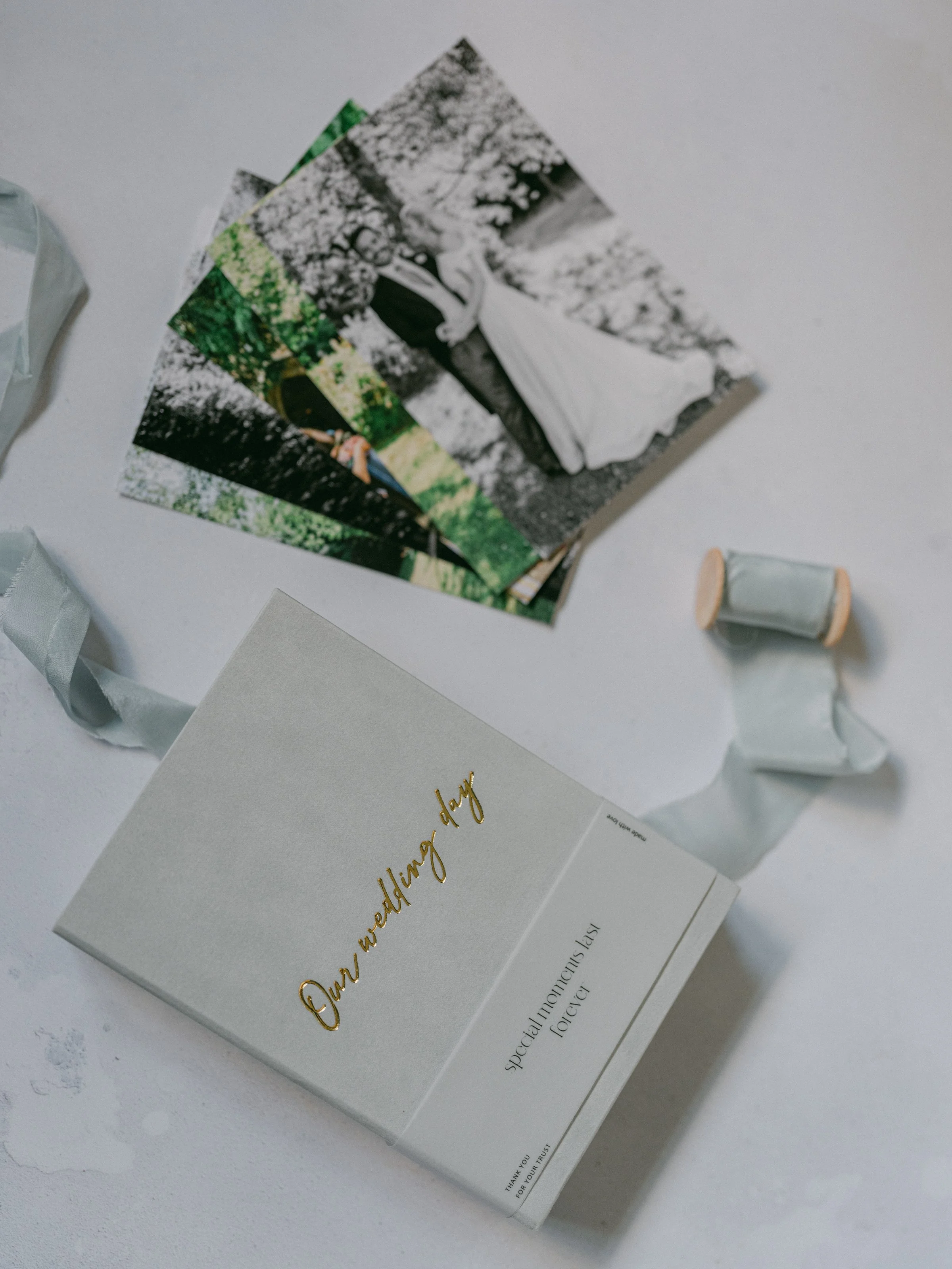 A wedding day card with a roll of ribbon, wedding photos, and a small box with golden text on the cover.