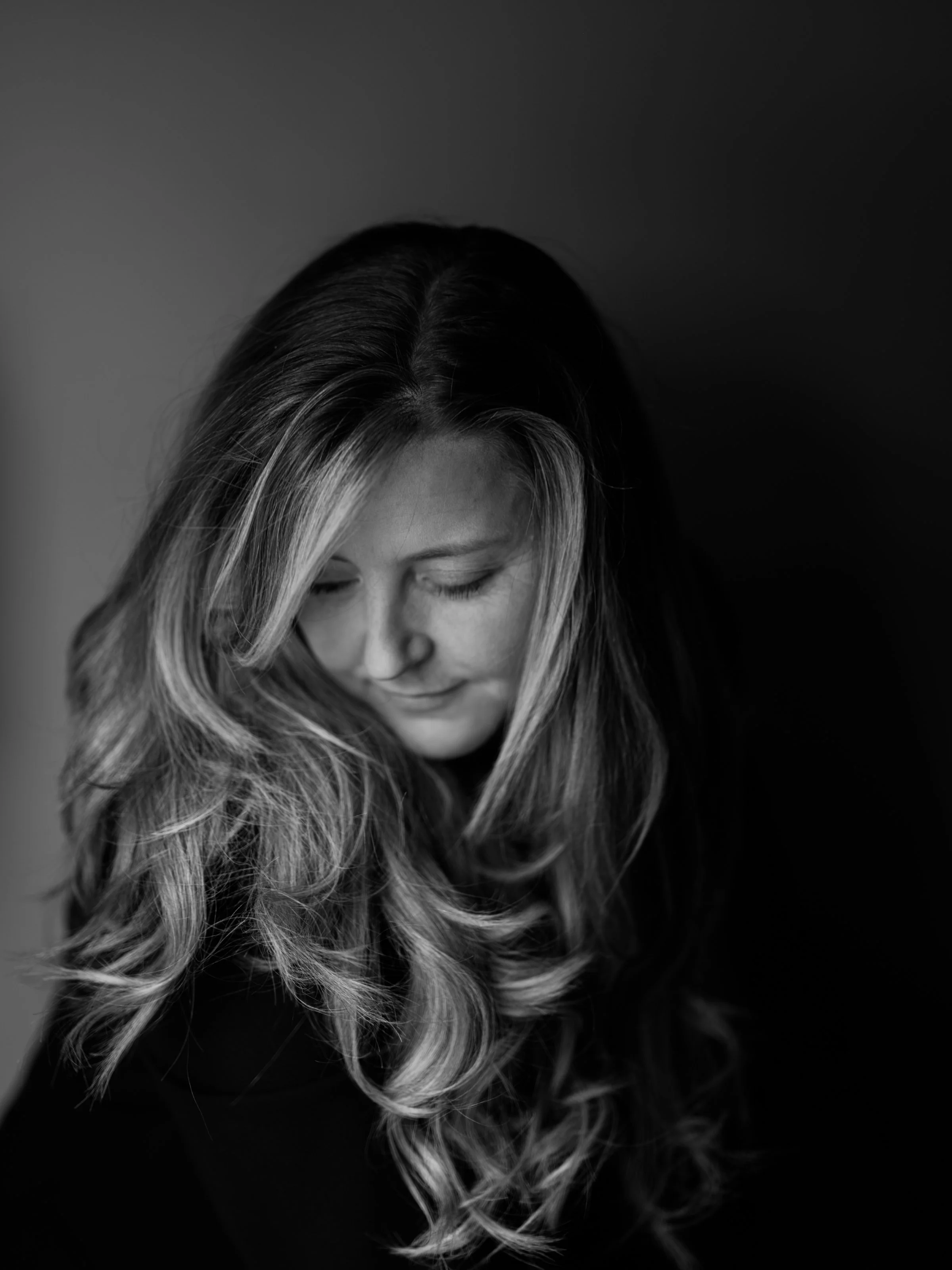 Black and white portrait of a woman with long, wavy hair and a gentle expression, looking downward with her eyes closed.