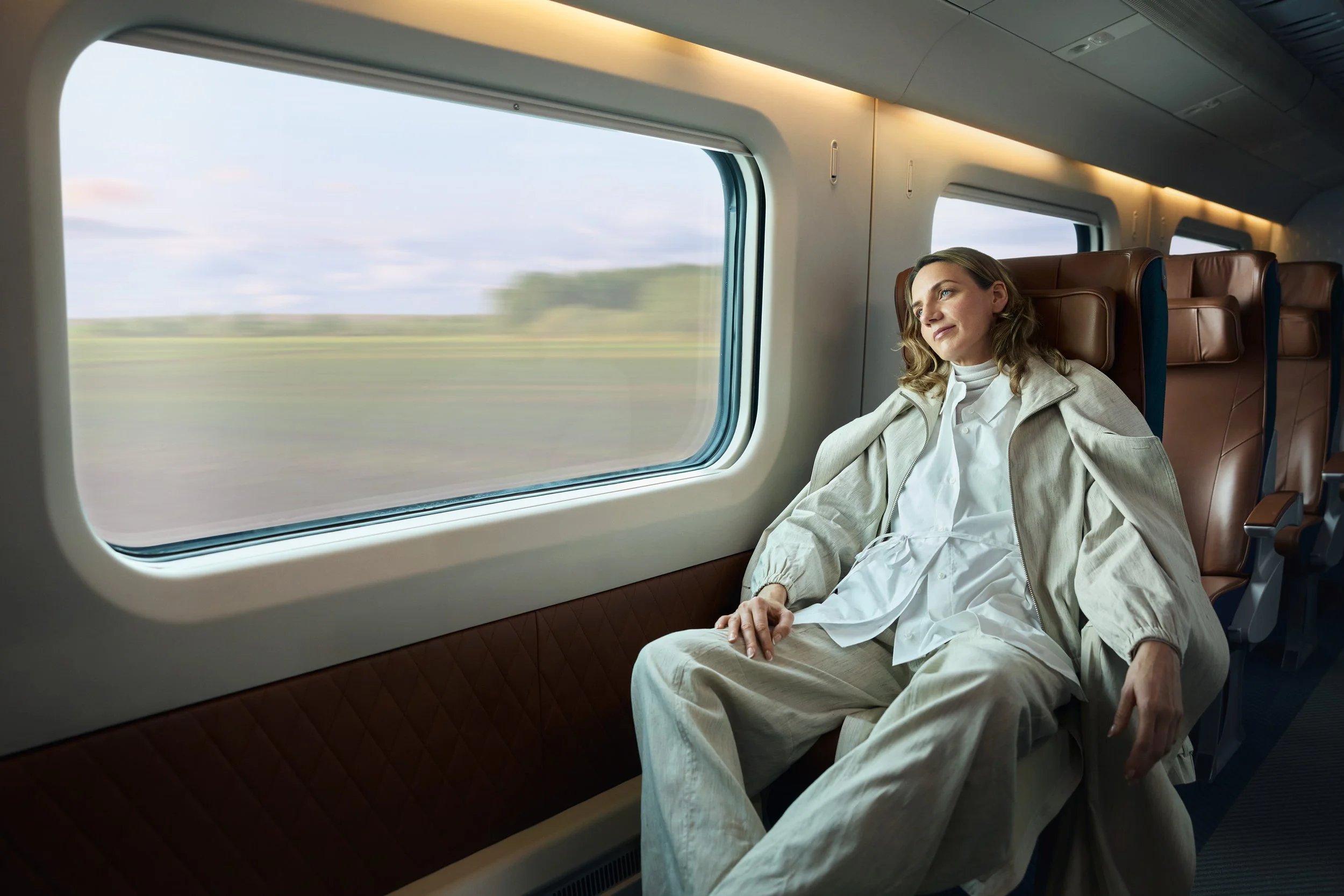 A woman sitting by a train window, looking outside with a contemplative expression.