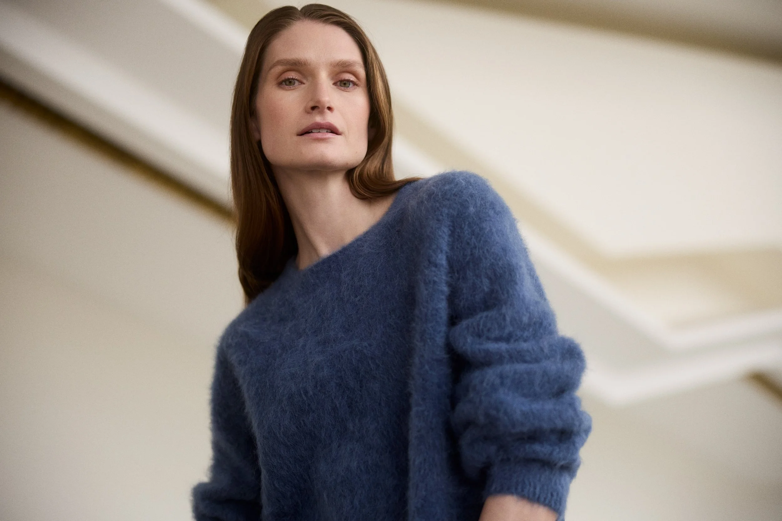 A woman with long brown hair wearing a cozy, fuzzy blue sweater, looking slightly to the side.