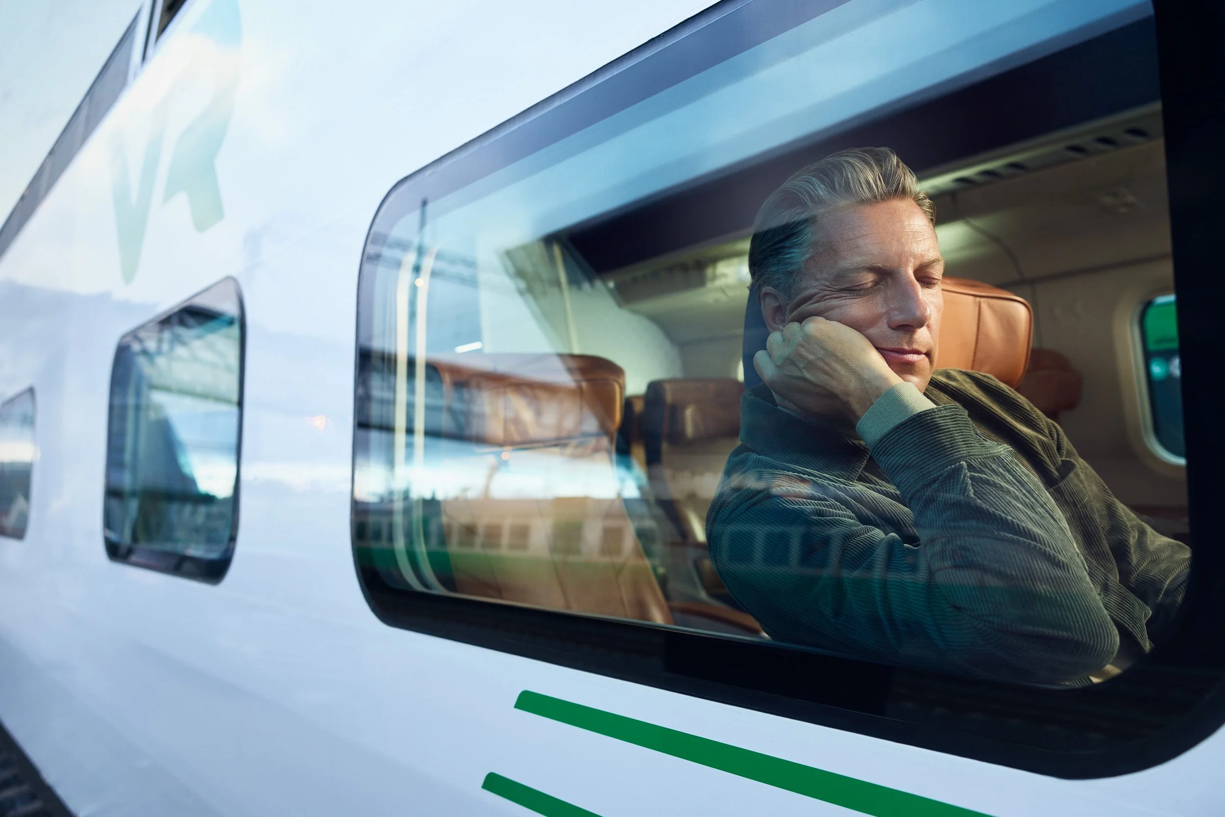 A man sleeping on an airplane, seen through the window with reflections of the sky and surroundings