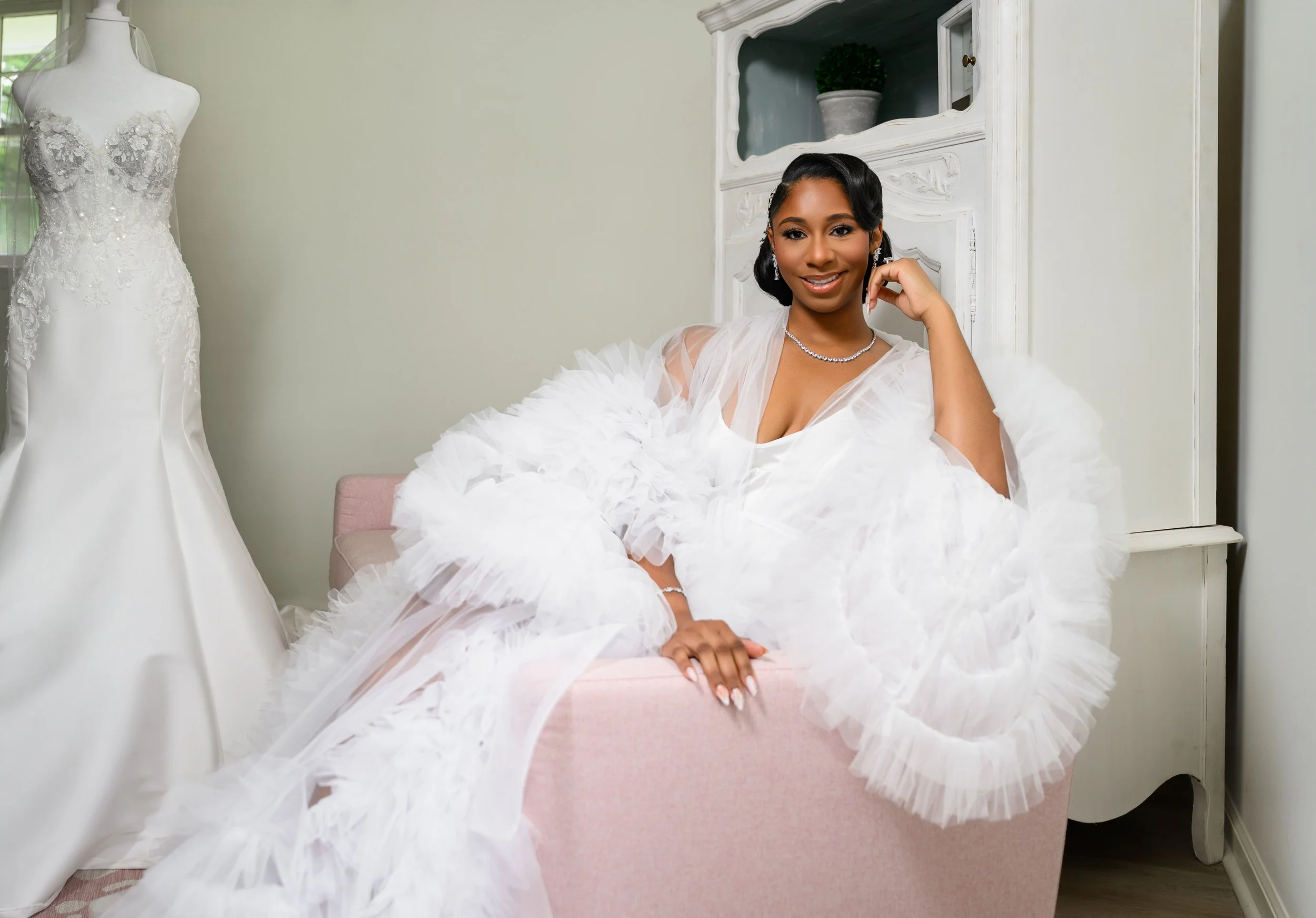 Bride seated in a white tulle robe beside her wedding gown while getting ready at The Venue at Daisy Hill.