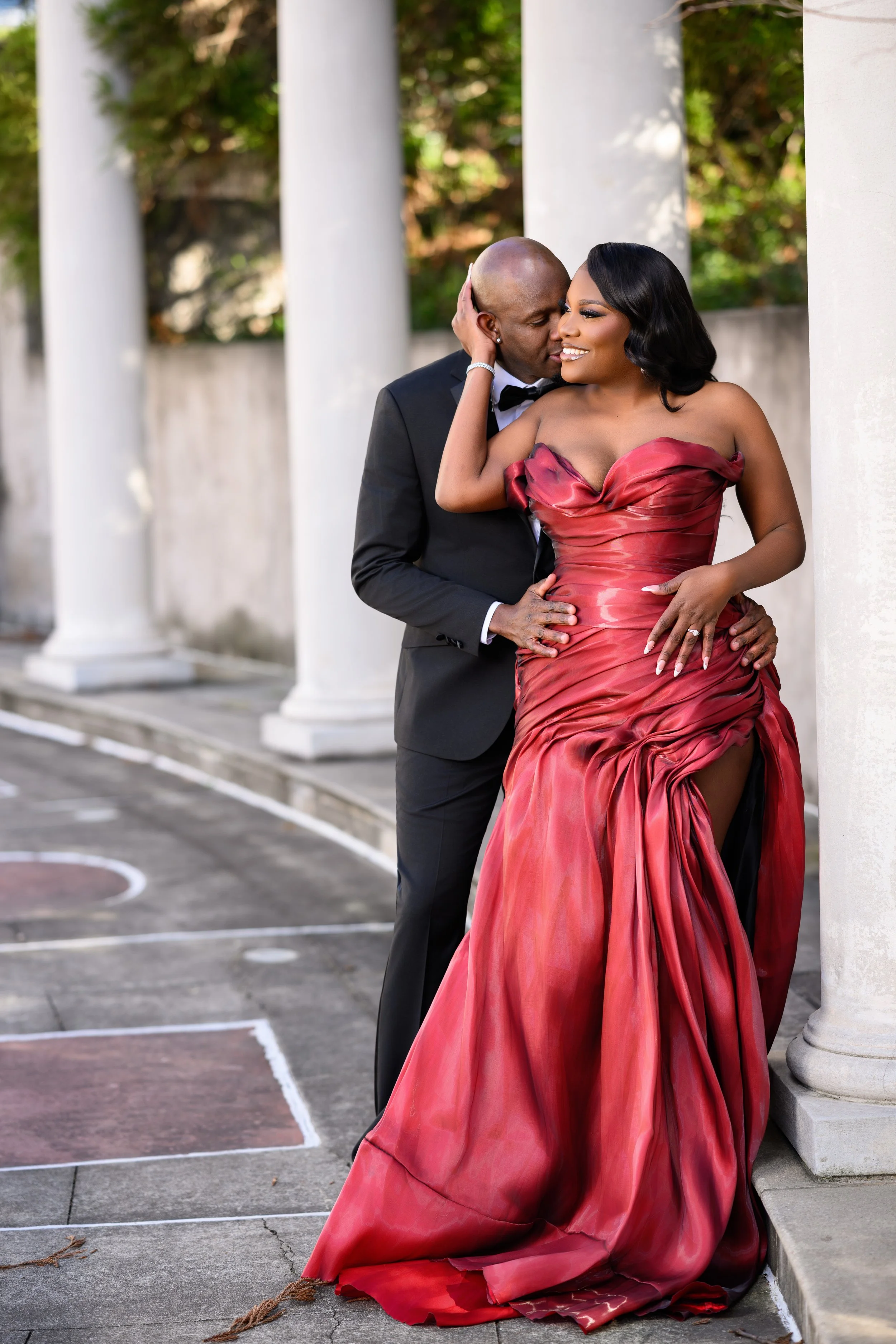 Intimate engagement moment with a couple embracing between white columns at Millennium Gate Museum on a cold day.