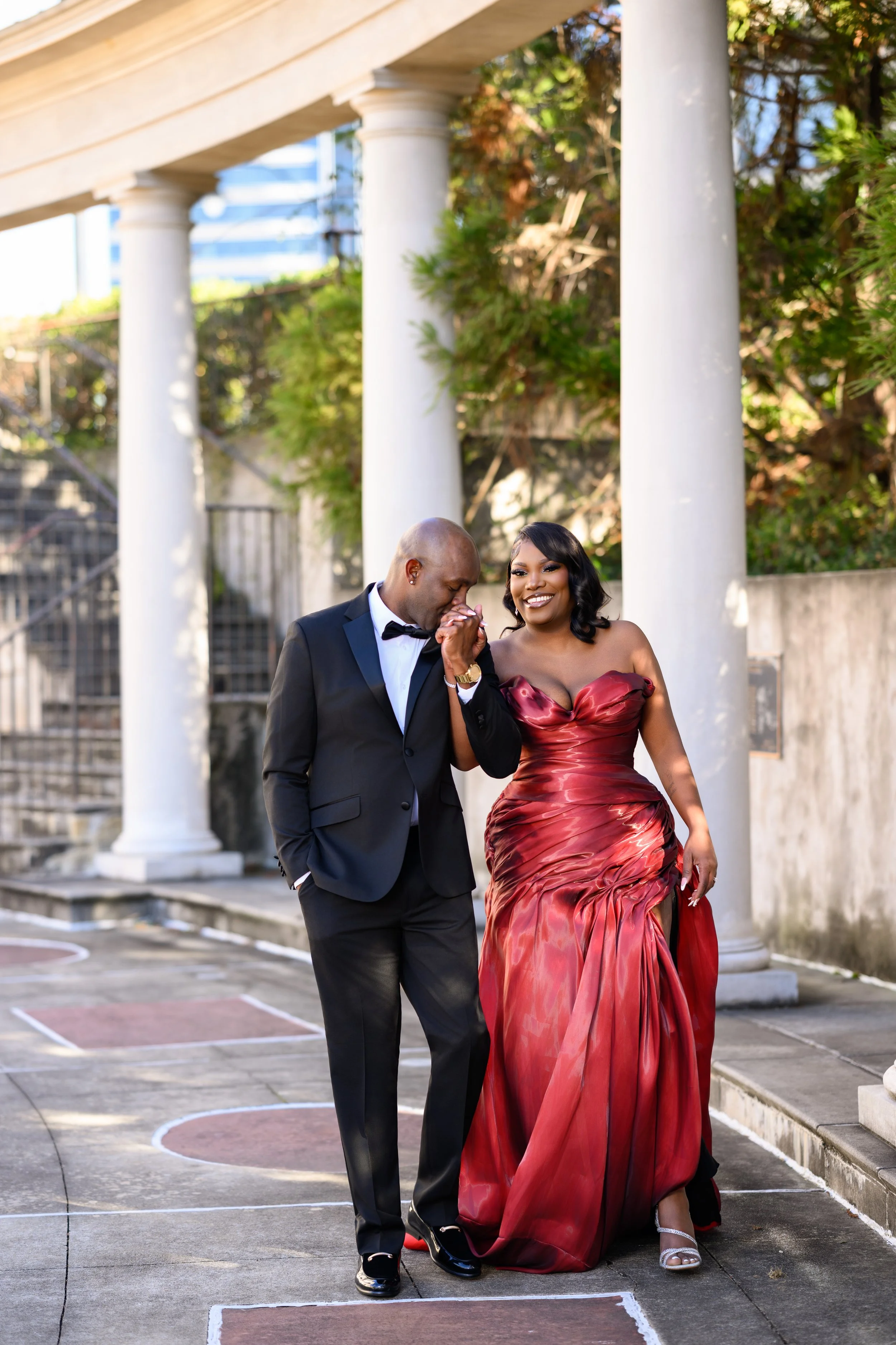 Joyful engagement session image of a couple holding hands and walking beneath the columns at Millennium Gate Museum in Atlanta.