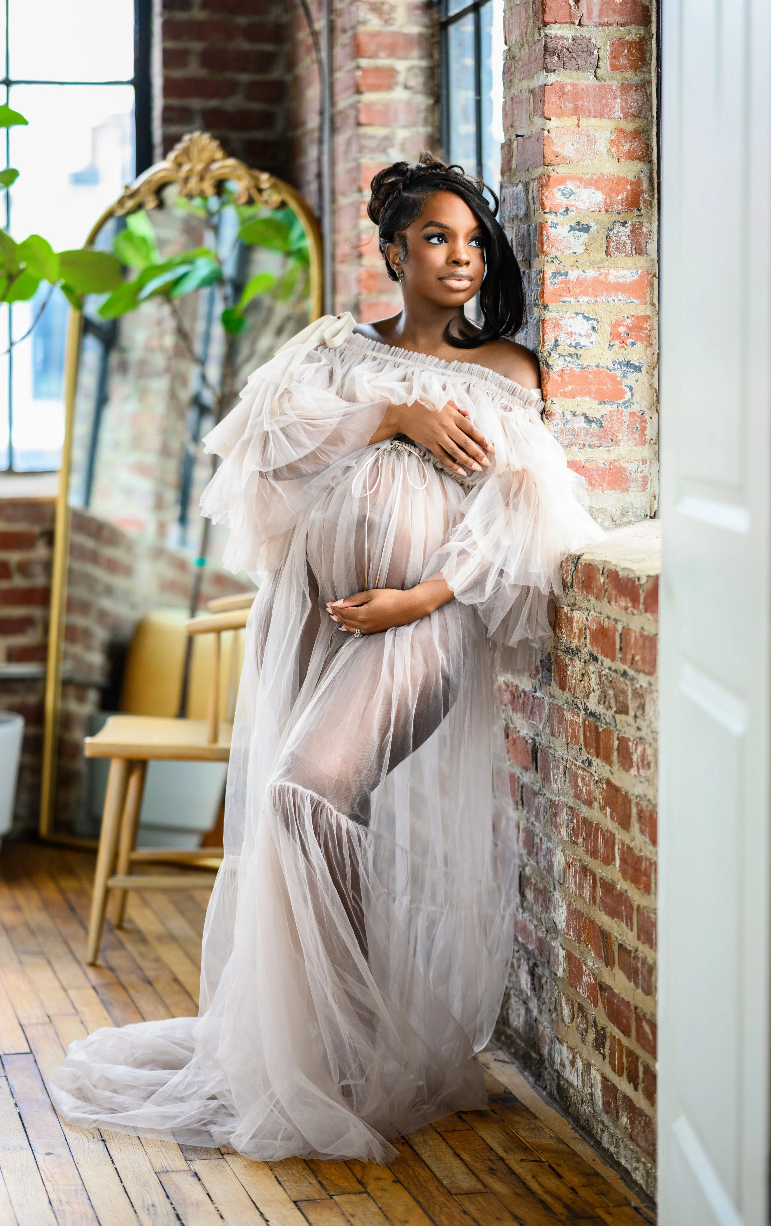 Expecting mother posing beside exposed brick and natural window light during a Midtown Atlanta maternity photography session.