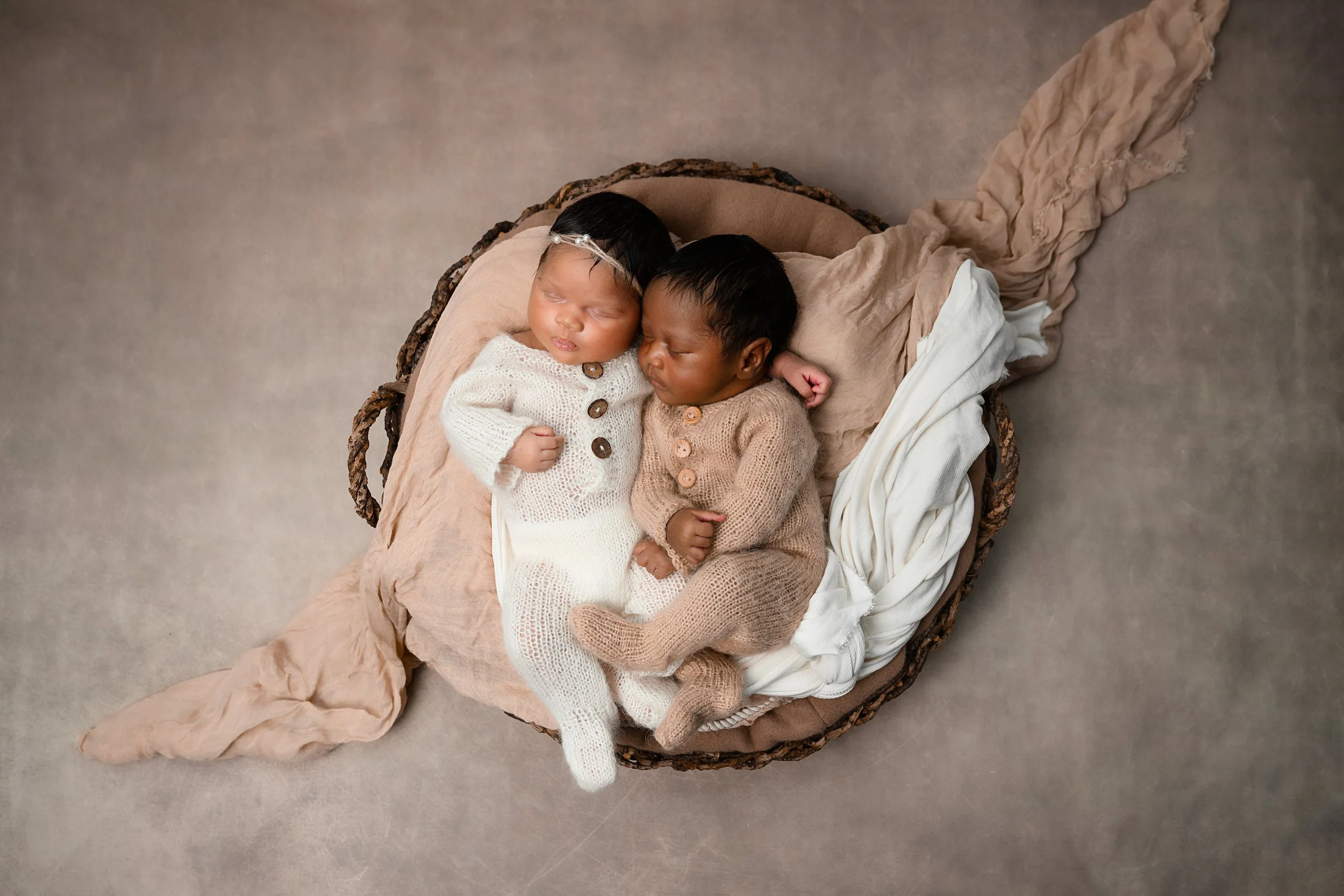 Newborn twins posed together in a rustic basket with cream and tan styling during an Atlanta newborn session.