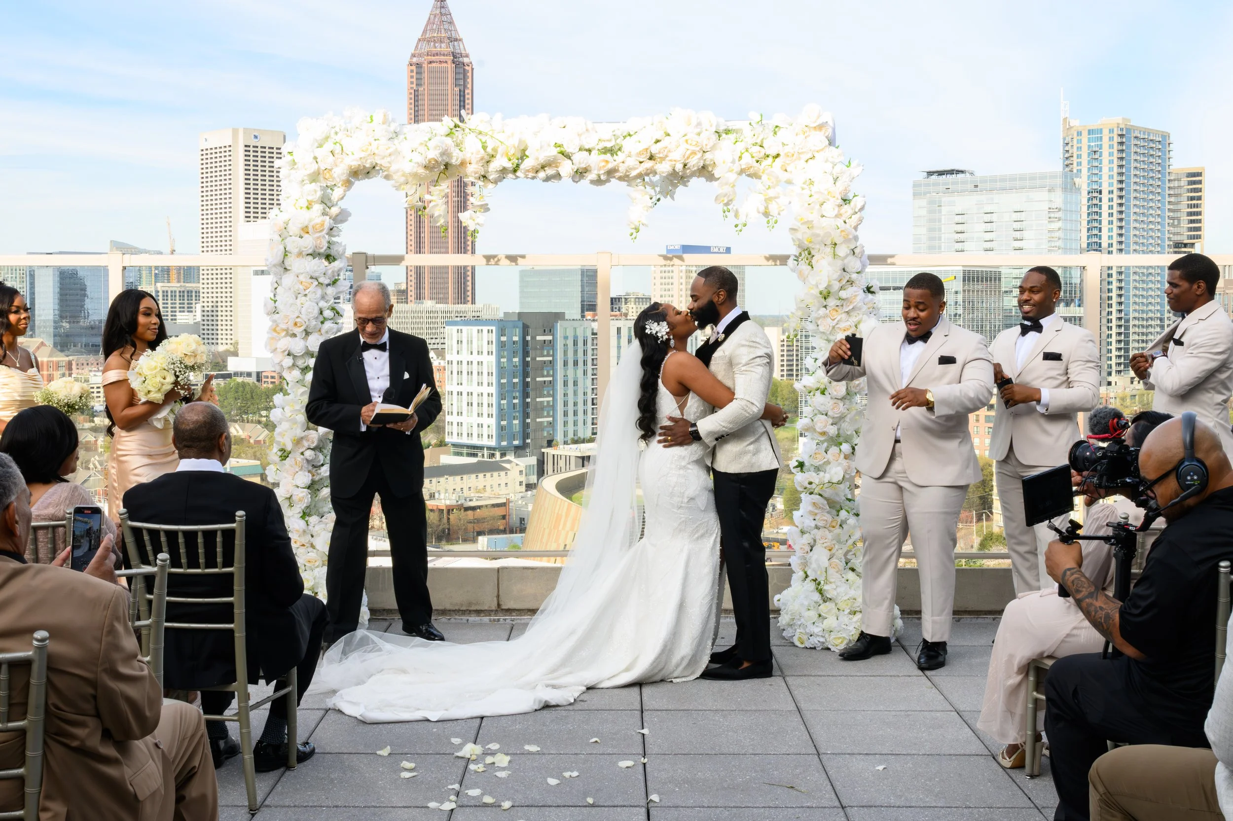 Newlyweds kissing beneath a floral arch with the Atlanta skyline behind them at Ventanas.