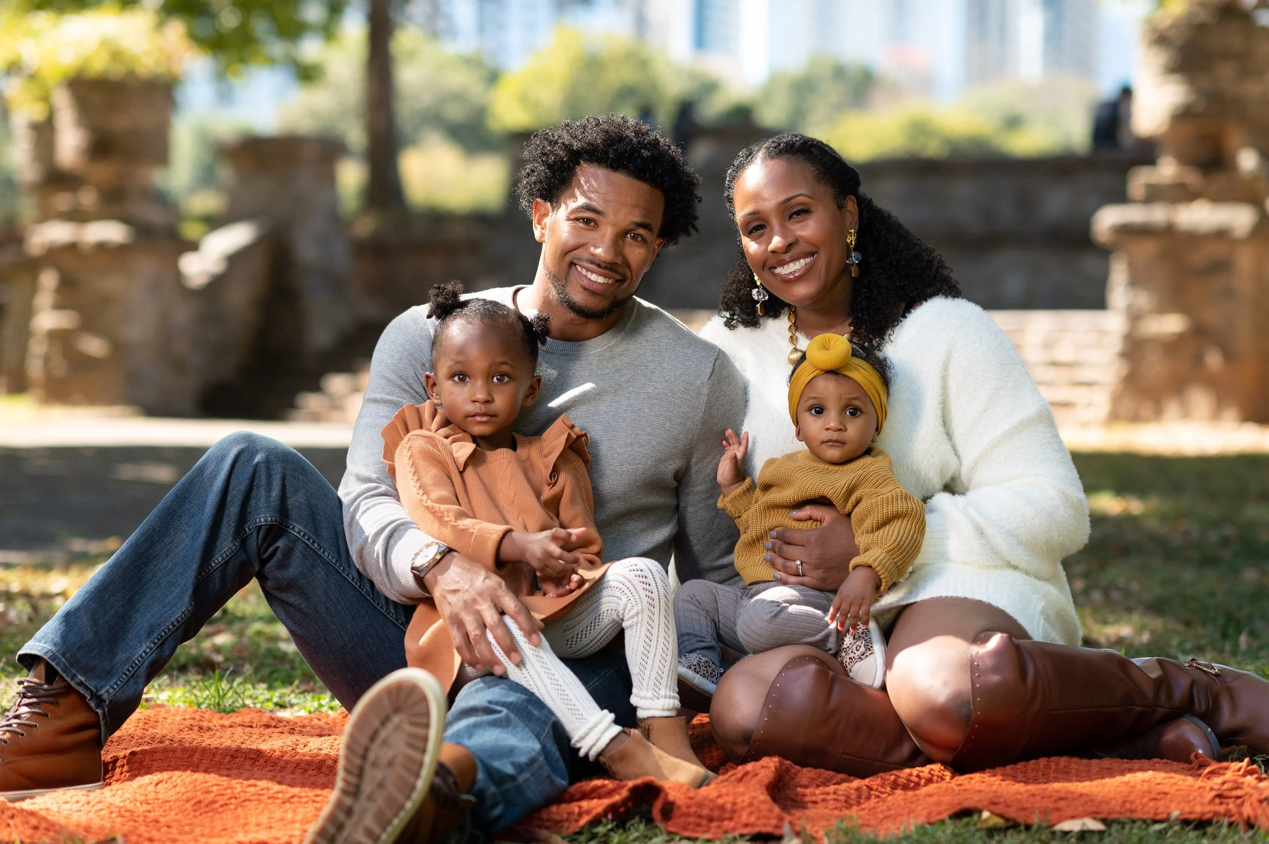 Family of four sitting together during an outdoor family portrait session at Piedmont Park in Atlanta, Georgia.