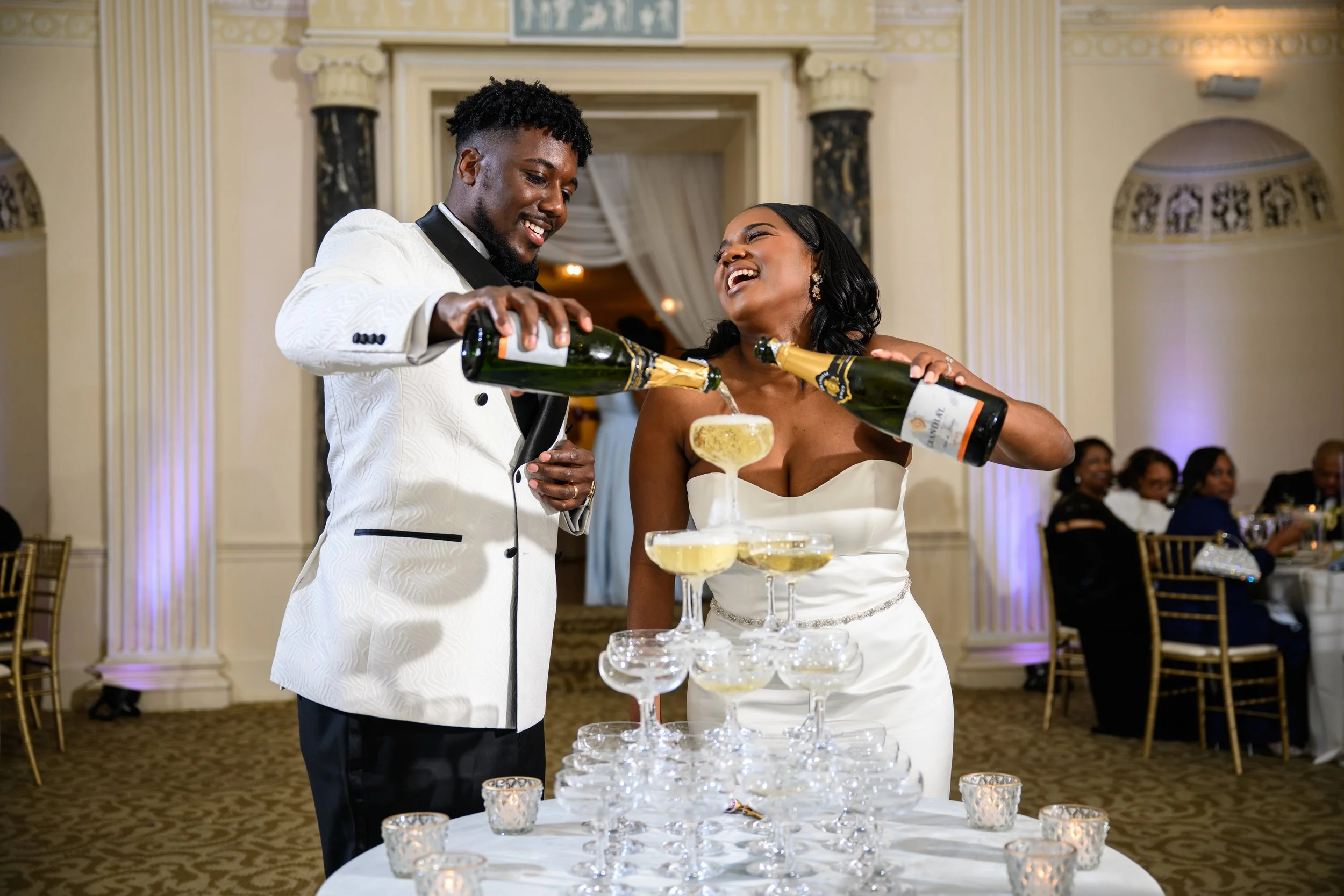 Bride and groom laughing while pouring champagne into a champagne tower during their wedding reception at The Biltmore in Atlanta, Georgia.