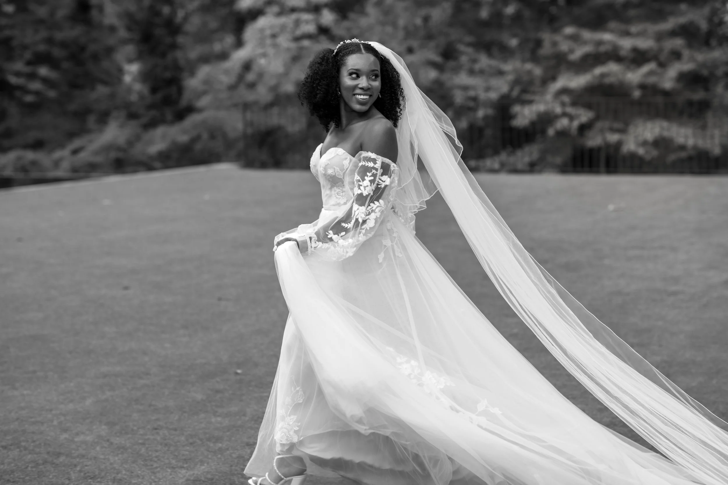 Bride smiles as her long wedding veil flows behind her during an outdoor bridal portrait.