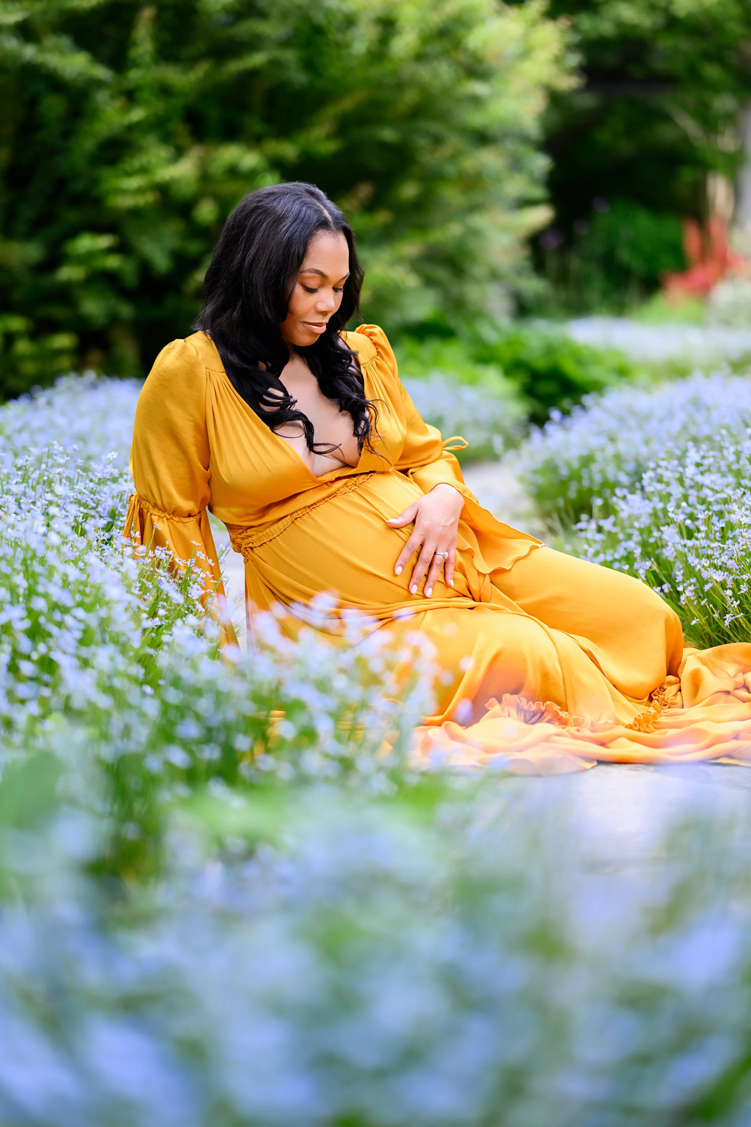 Mother-to-be cradling her baby bump while seated among flowers during an outdoor maternity portrait session.