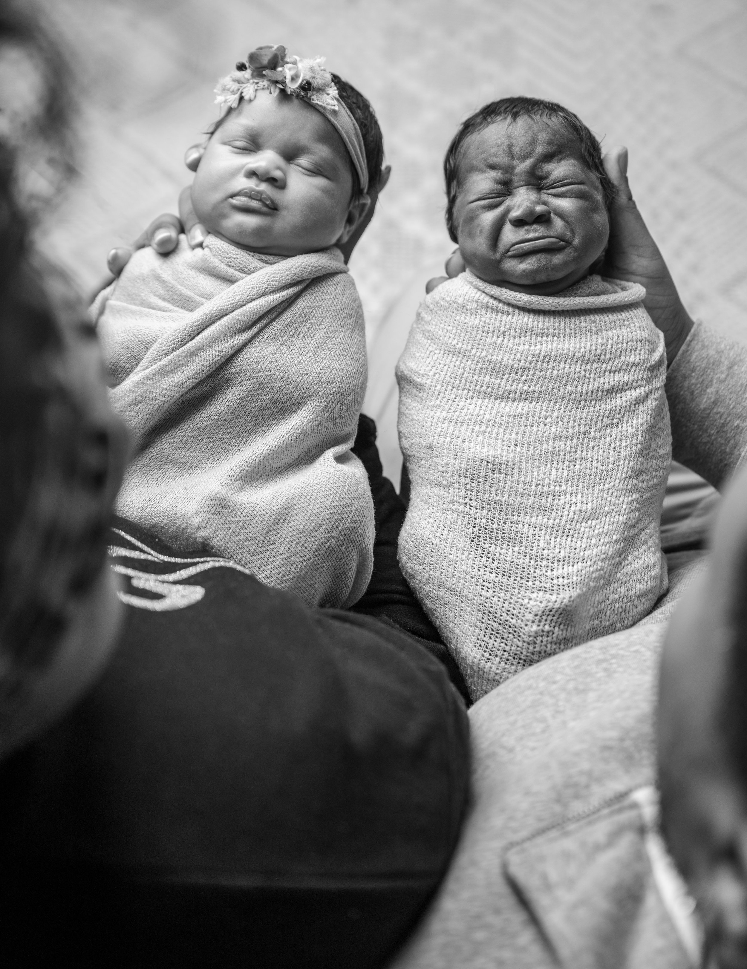 Black-and-white portrait of newborn twins being held during their newborn photography session.