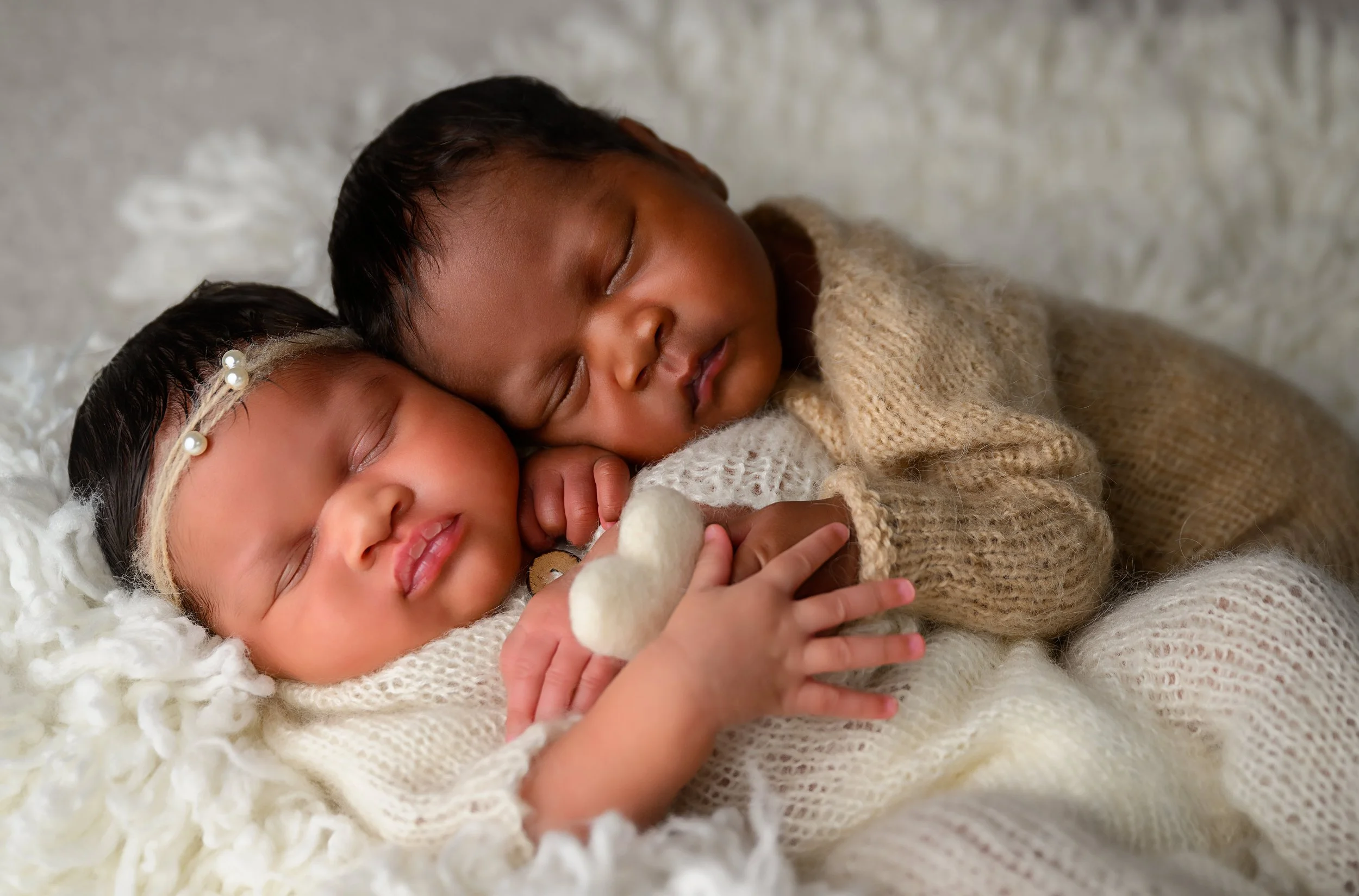 Newborn twins sleeping together in coordinating cream and tan knit outfits during an Atlanta newborn photography session.