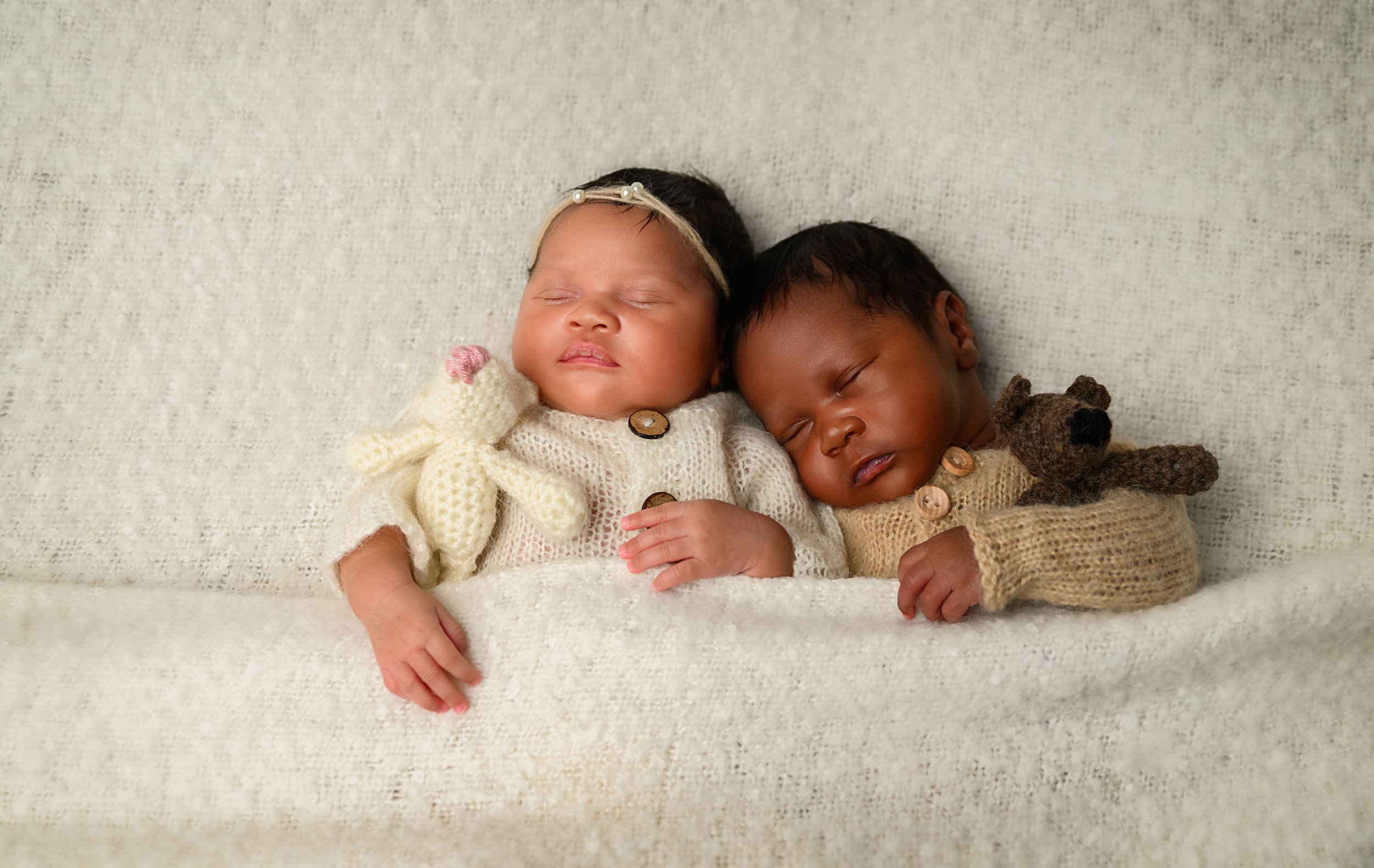Newborn twins posed together with small knit toys in a soft neutral newborn photography setup.