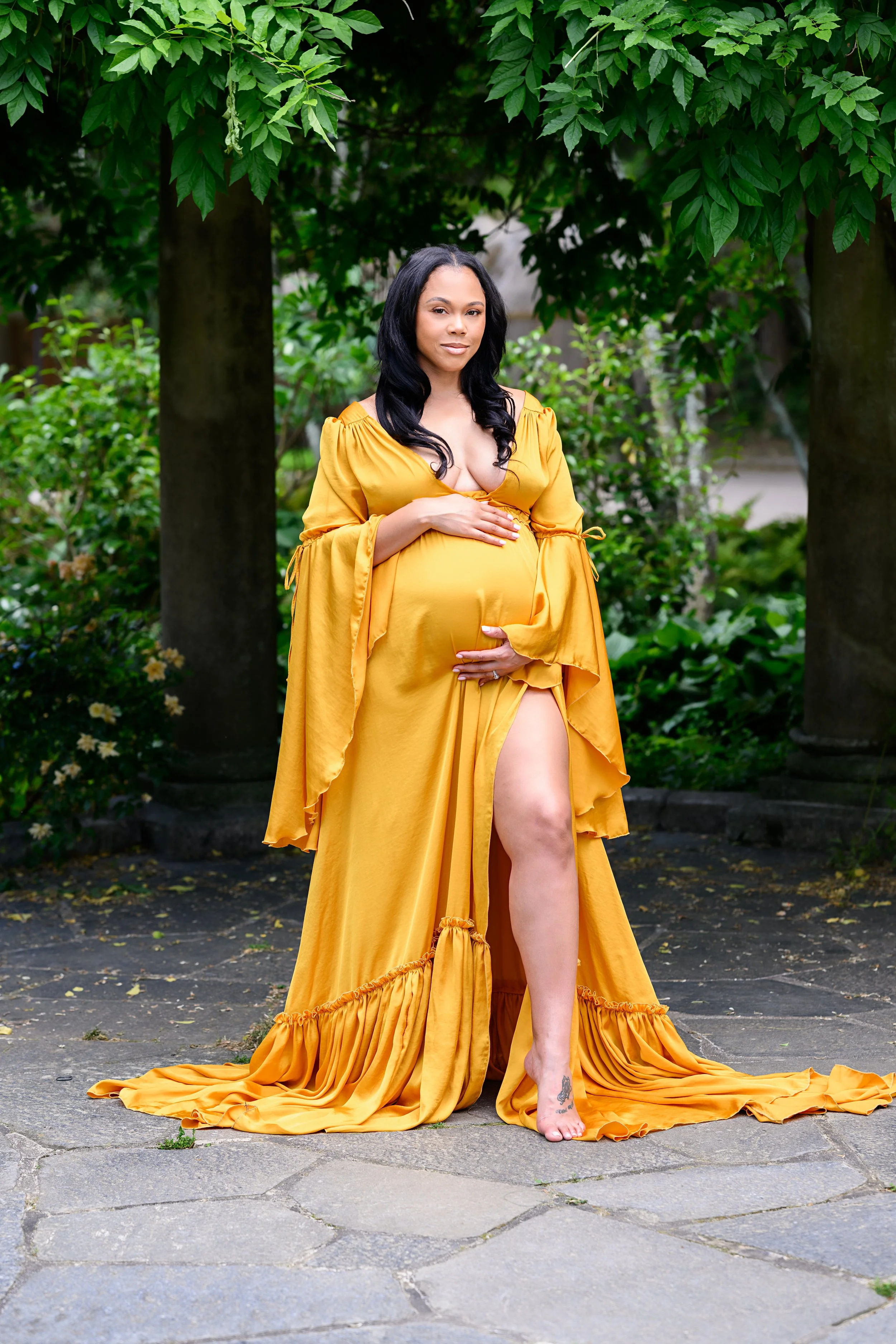 Full-length maternity portrait of an expectant mother wearing a golden gown in an Atlanta garden setting.