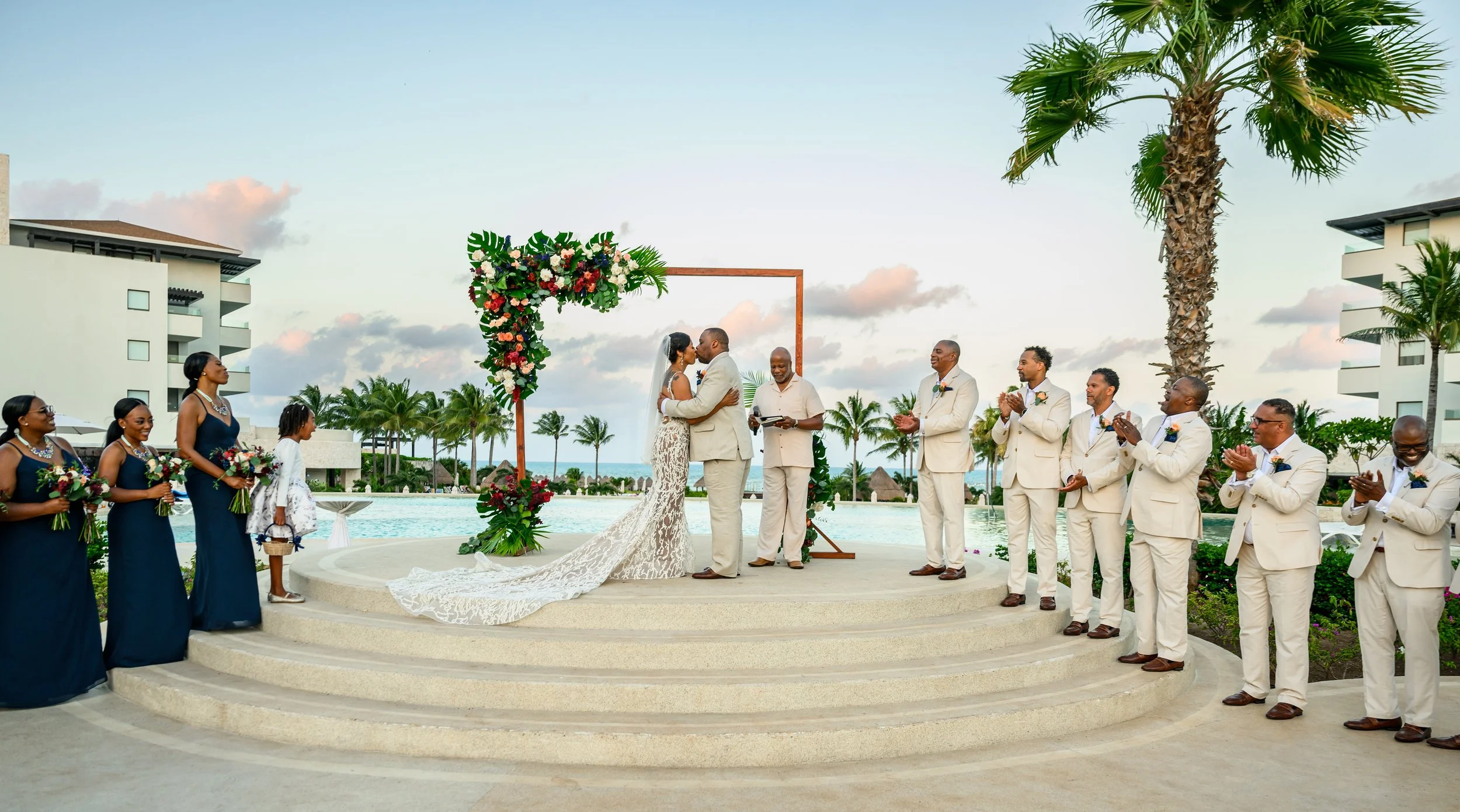 Tekla and Rick exchanging vows beneath a colorful floral arch during their Cancun wedding.