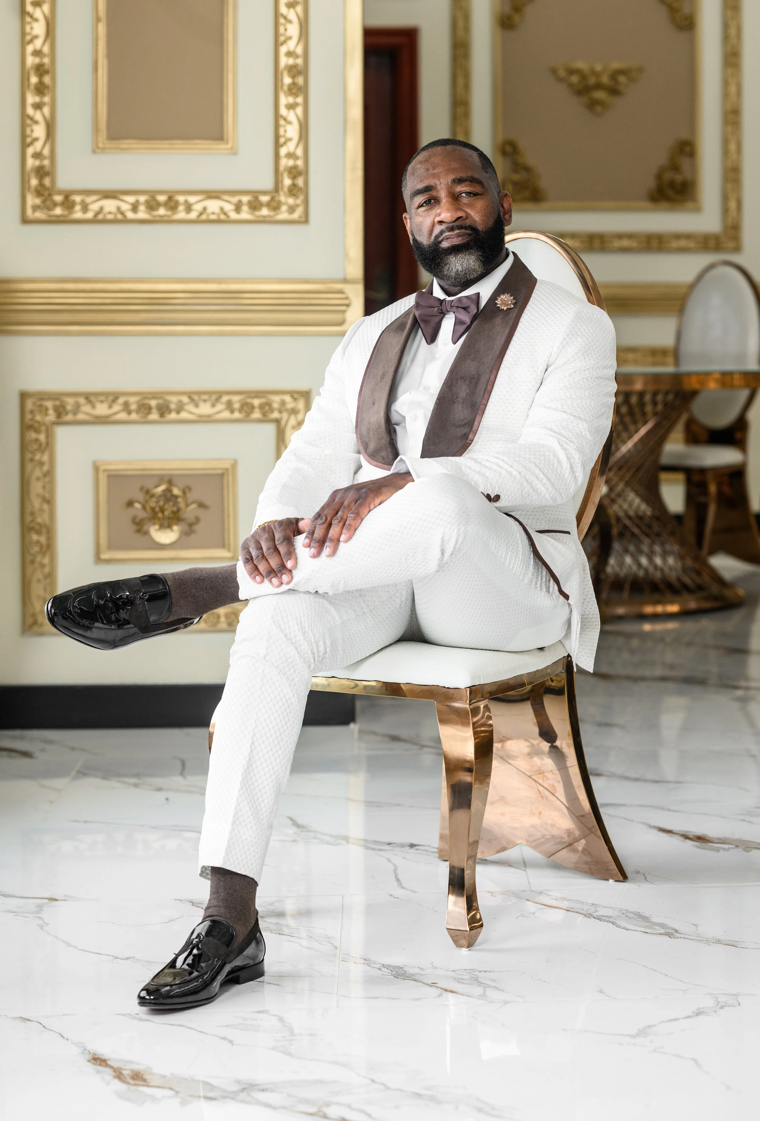 Groom in a white and brown tuxedo seated for a wedding portrait at Shahbain Events Center.