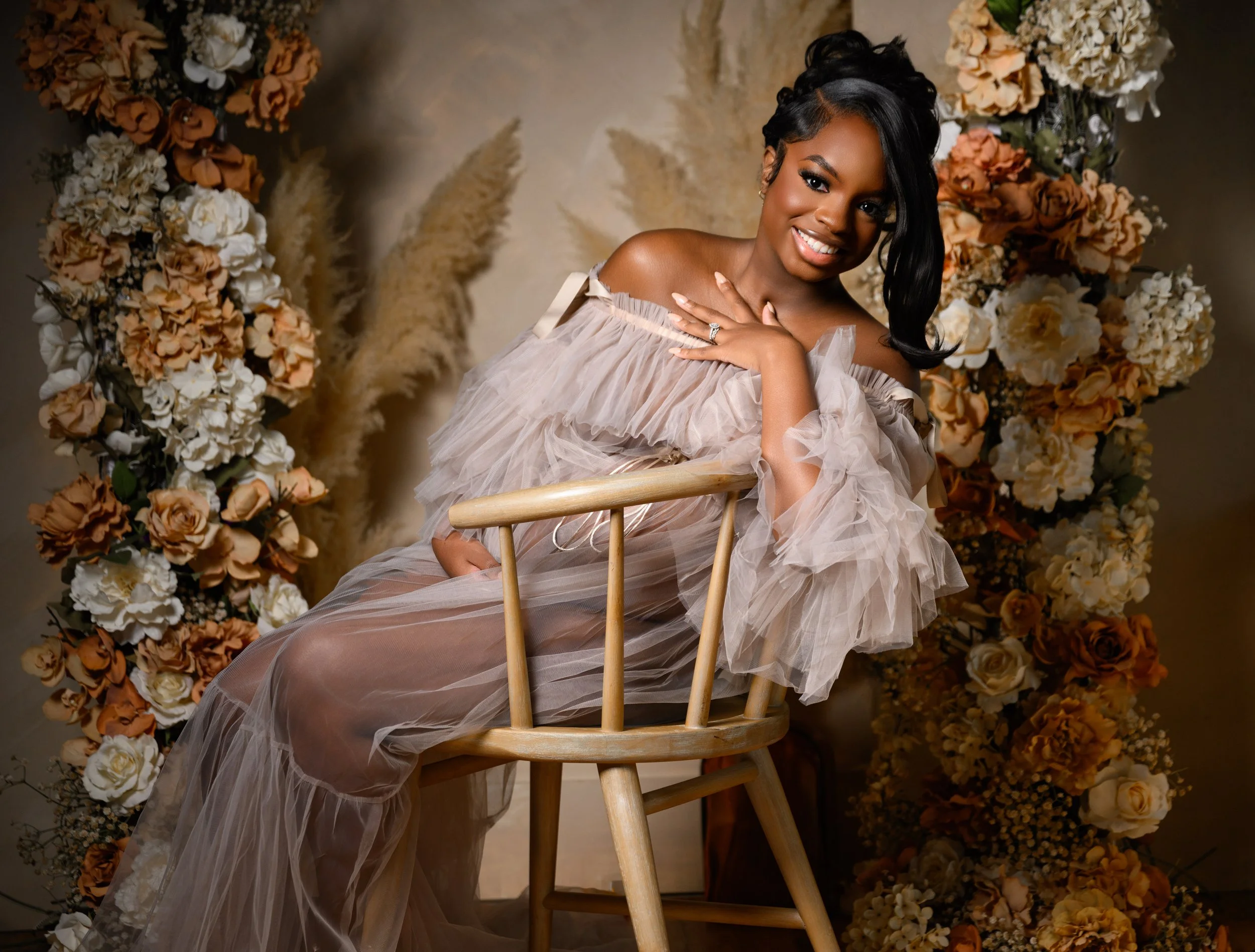 Seated maternity portrait featuring a flowing neutral gown and floral backdrop in a Midtown Atlanta photography studio.