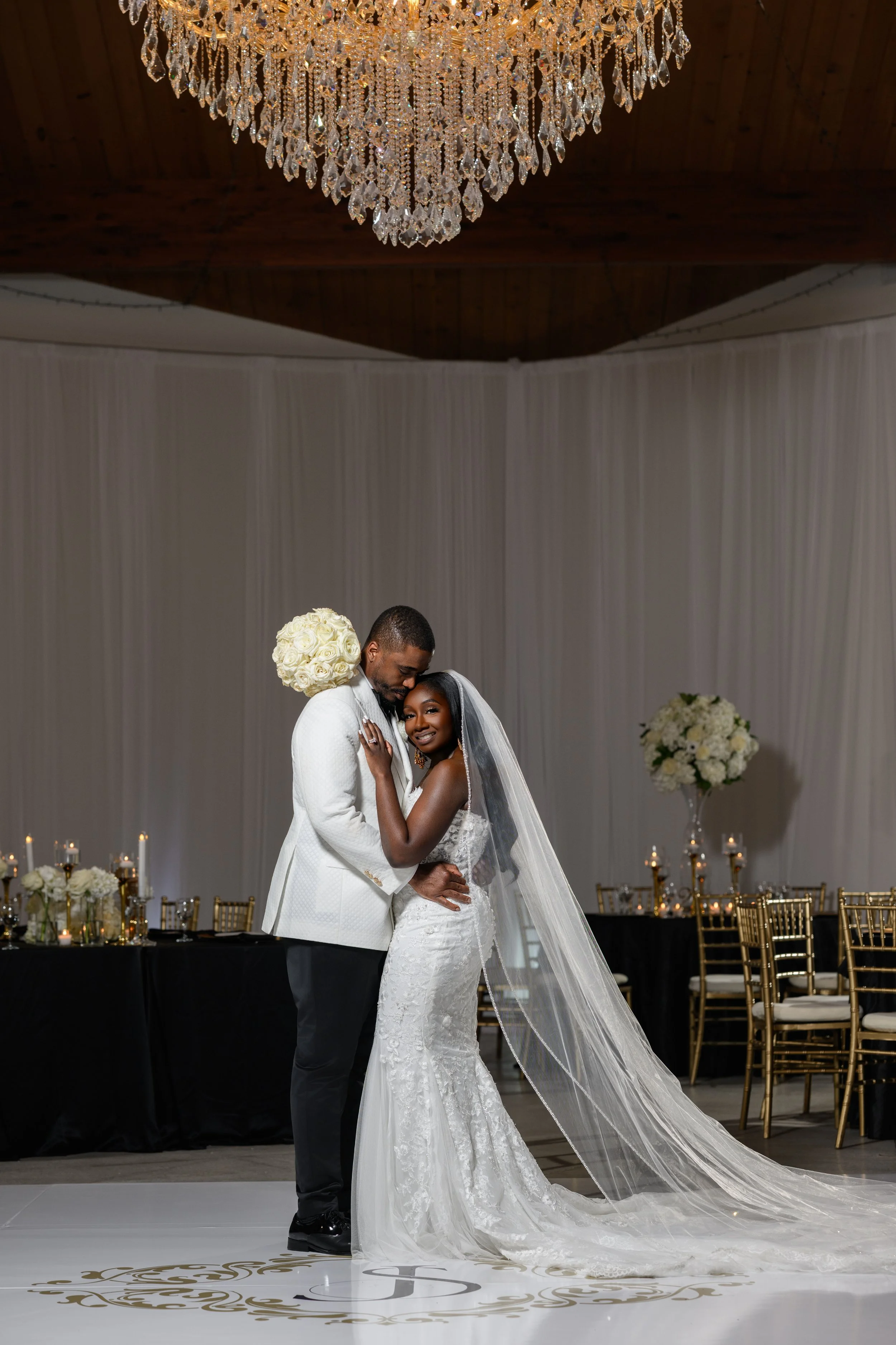 Bride and groom embracing beneath a crystal chandelier during their wedding reception at The West Venue in Atlanta, photographed by Crystal Artis Photography.