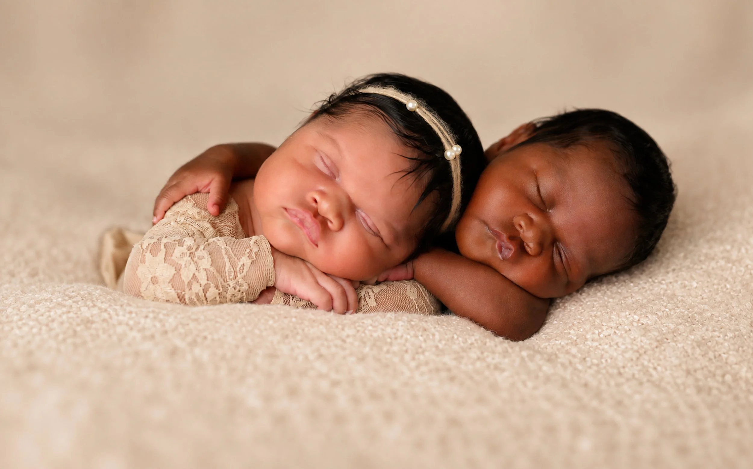 A sweet newborn twin portrait featuring the J Twins sleeping closely together against a soft cream backdrop, photographed by Crystal Artis Photography in Atlanta.