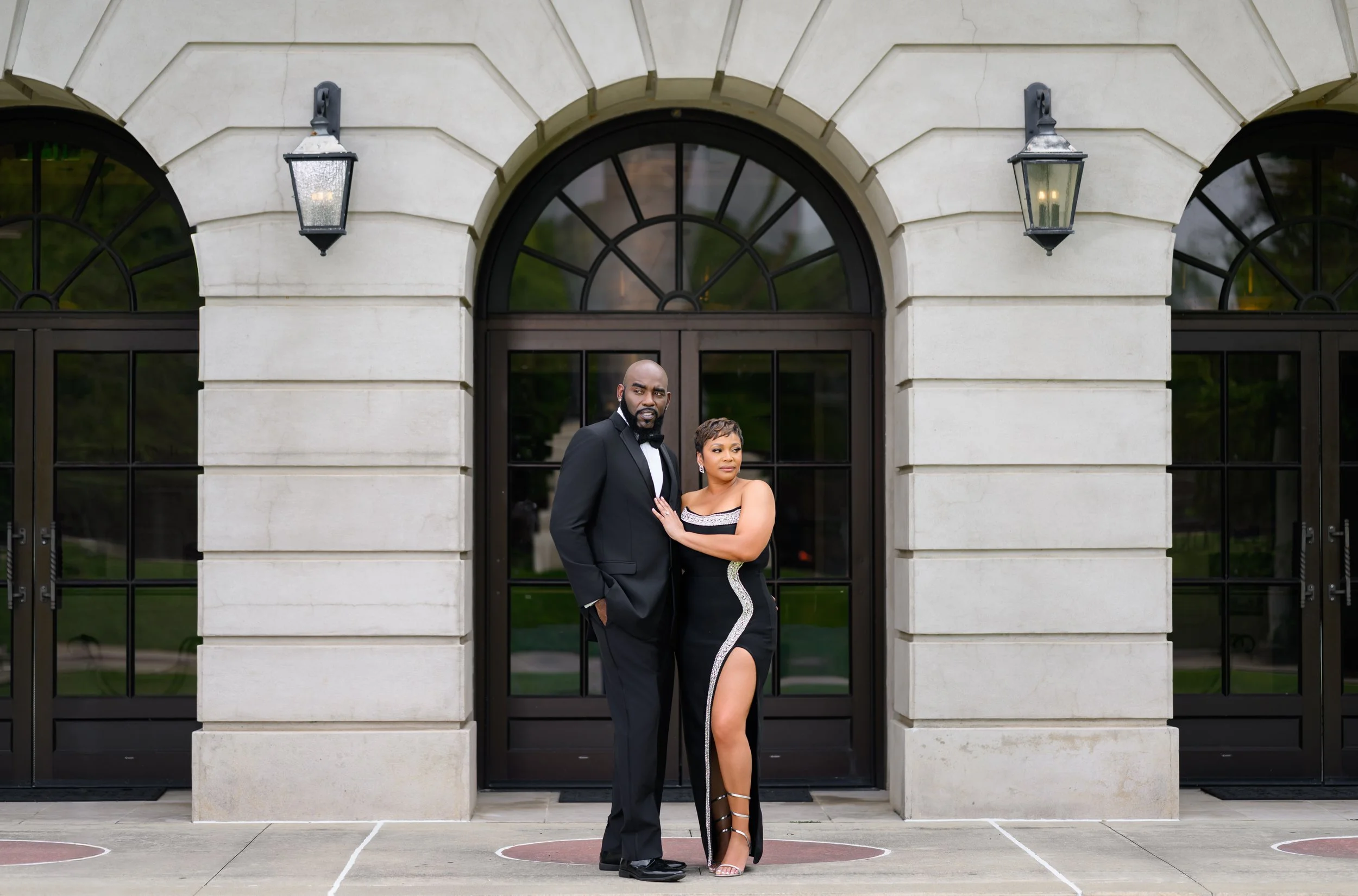 Engaged couple dressed in formal black attire posing outside an Atlanta venue, photographed by Crystal Artis Photography.