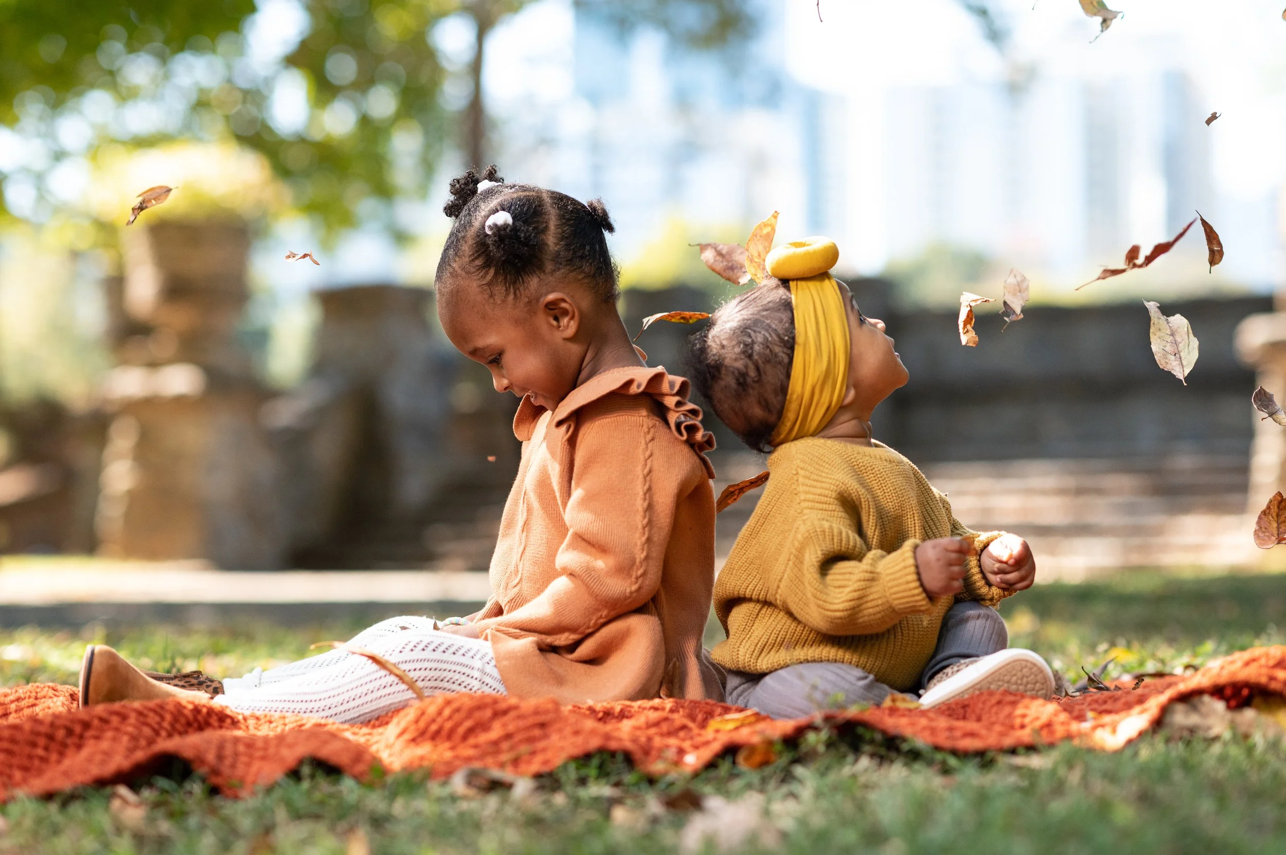 Two sisters playing with fall leaves during a family photography session at Piedmont Park in Atlanta.