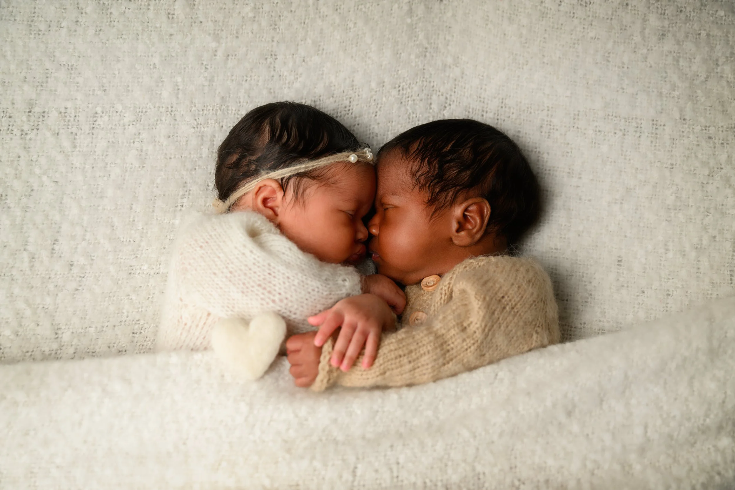 Newborn twins sleeping nose-to-nose in coordinating neutral outfits during their newborn portrait session.
