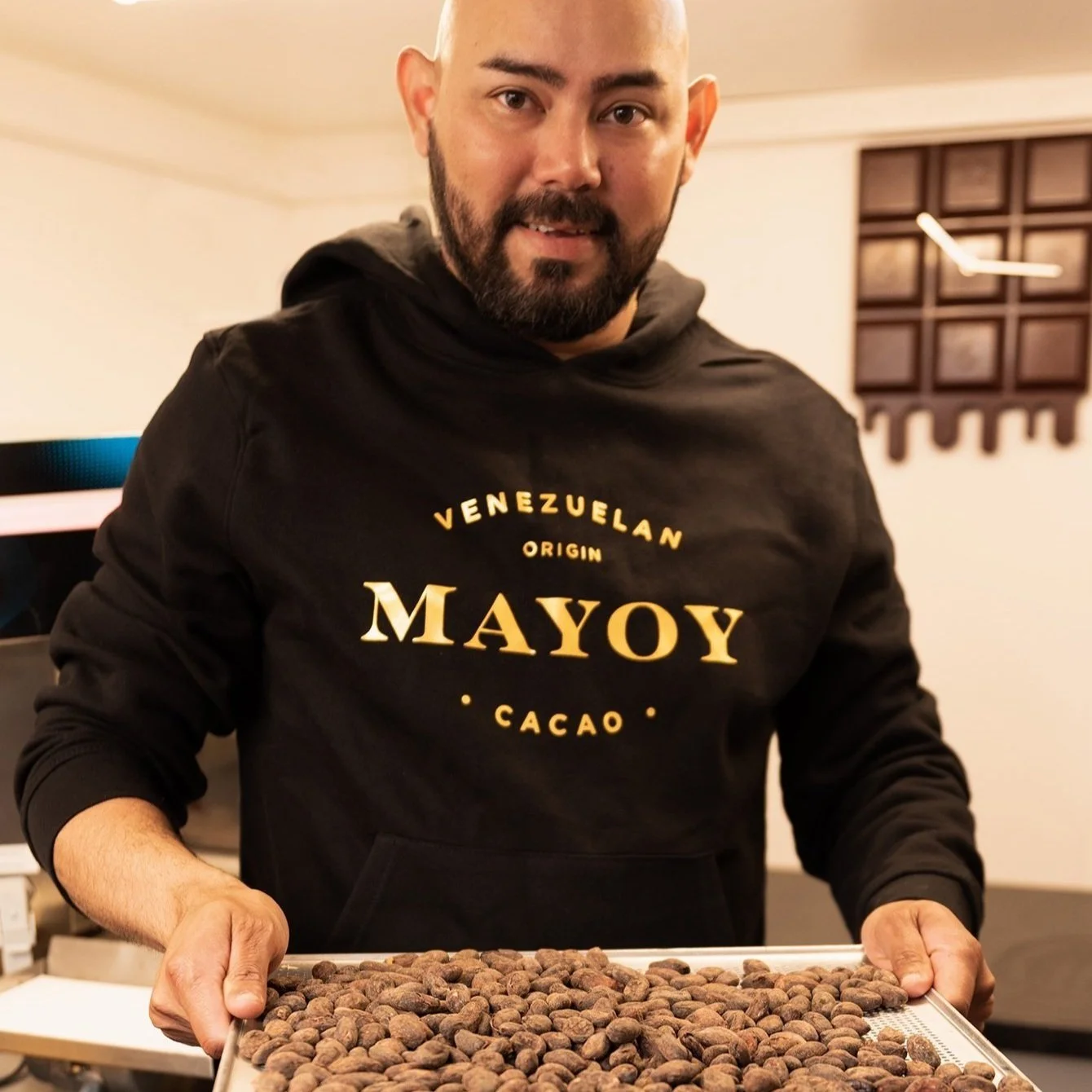 Chocolate-maker, holding cacao tray, smiles looking at camera