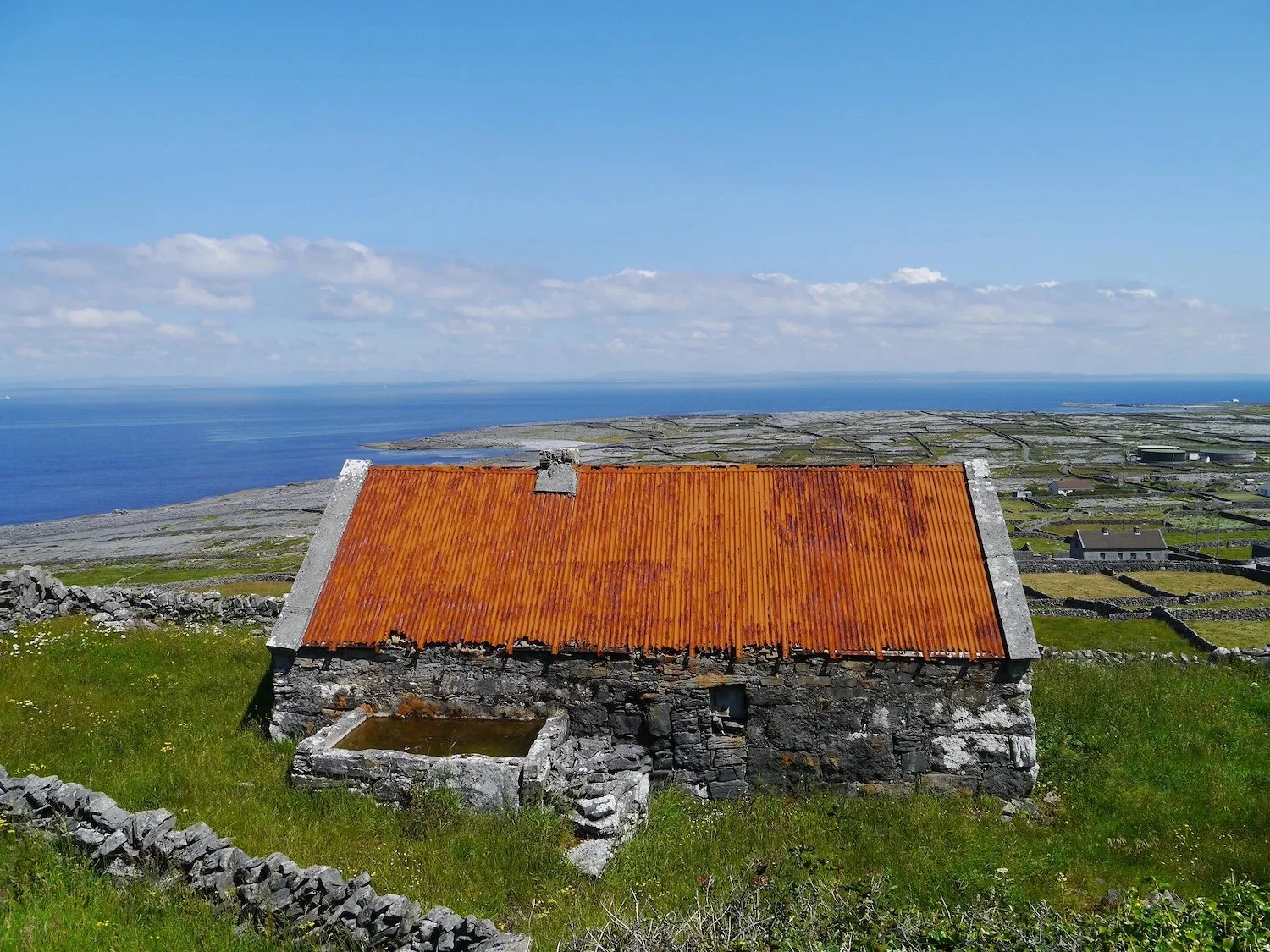 Stone building with rusted corrugated metal roof. Landscape of Aran Islands, Ireland in background.