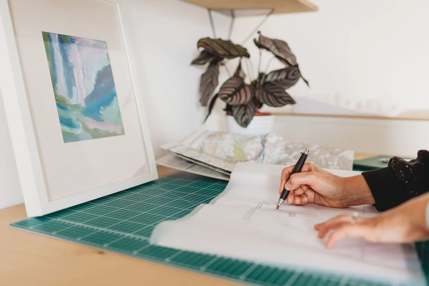 Architect drawing on tracing paper with plant, painting and map in background
