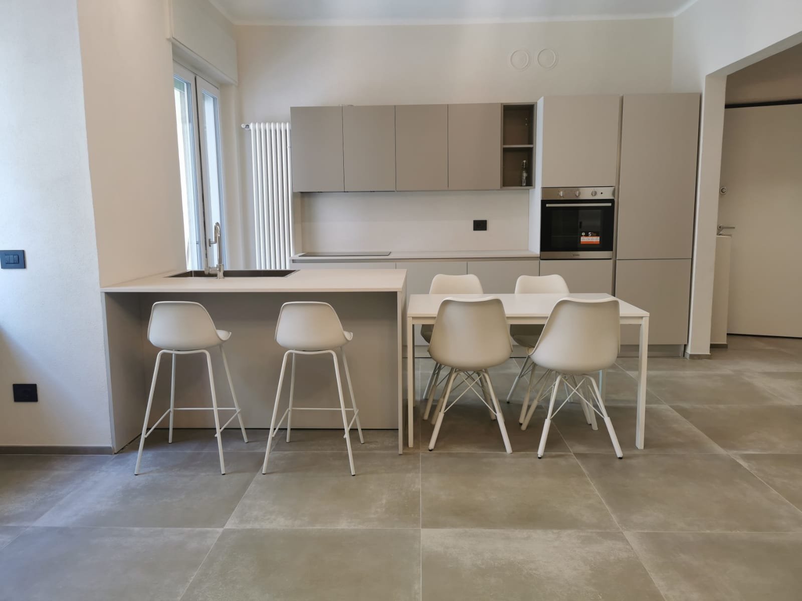 Cucina moderna con piano di lavoro bianco, sedie bianche e armadi beige
