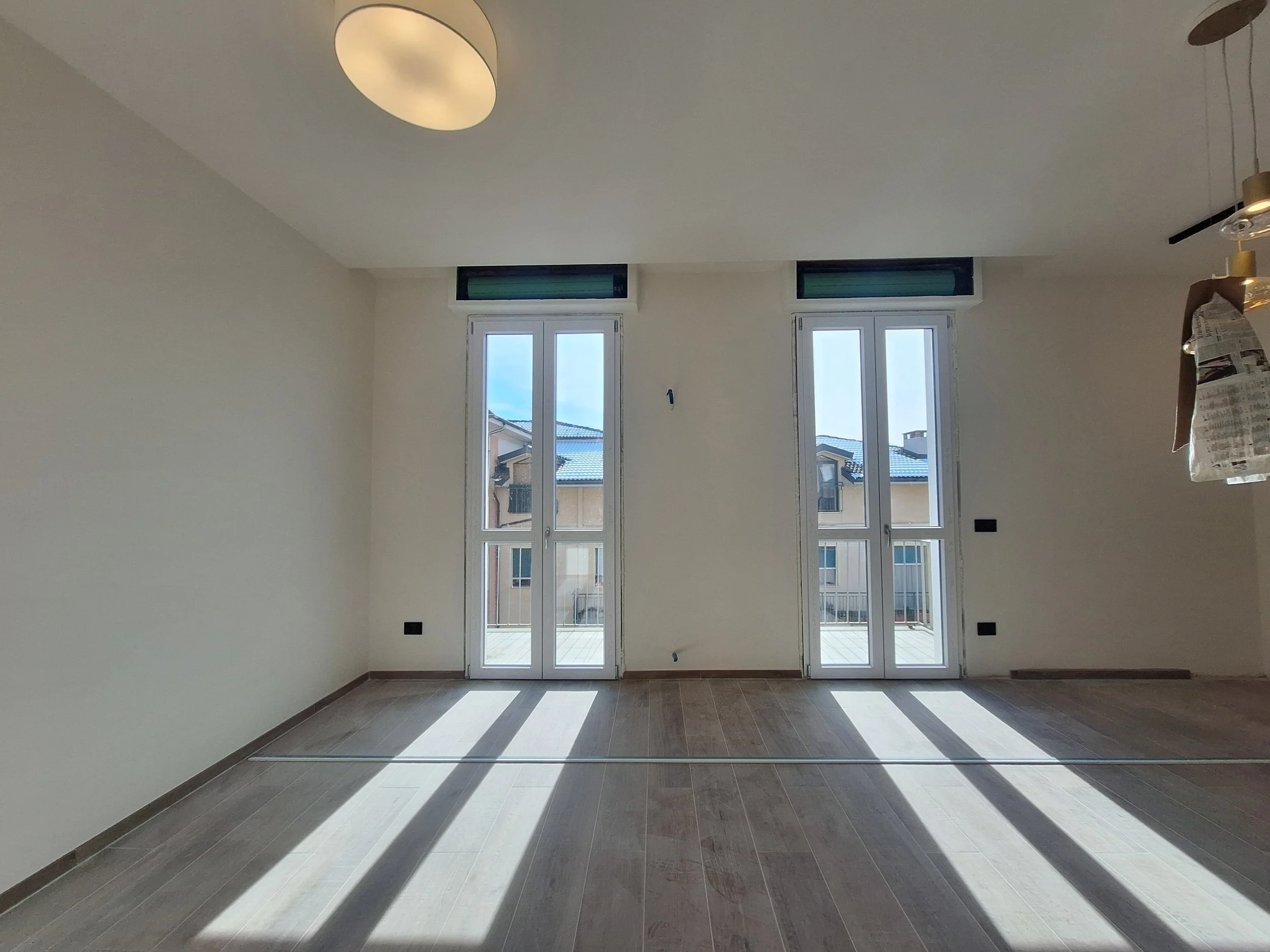 Stanza vuota in fase di costruzione, con due grandi porte-finestra che si affacciano su un balcone e lasciando entrare molta luce.