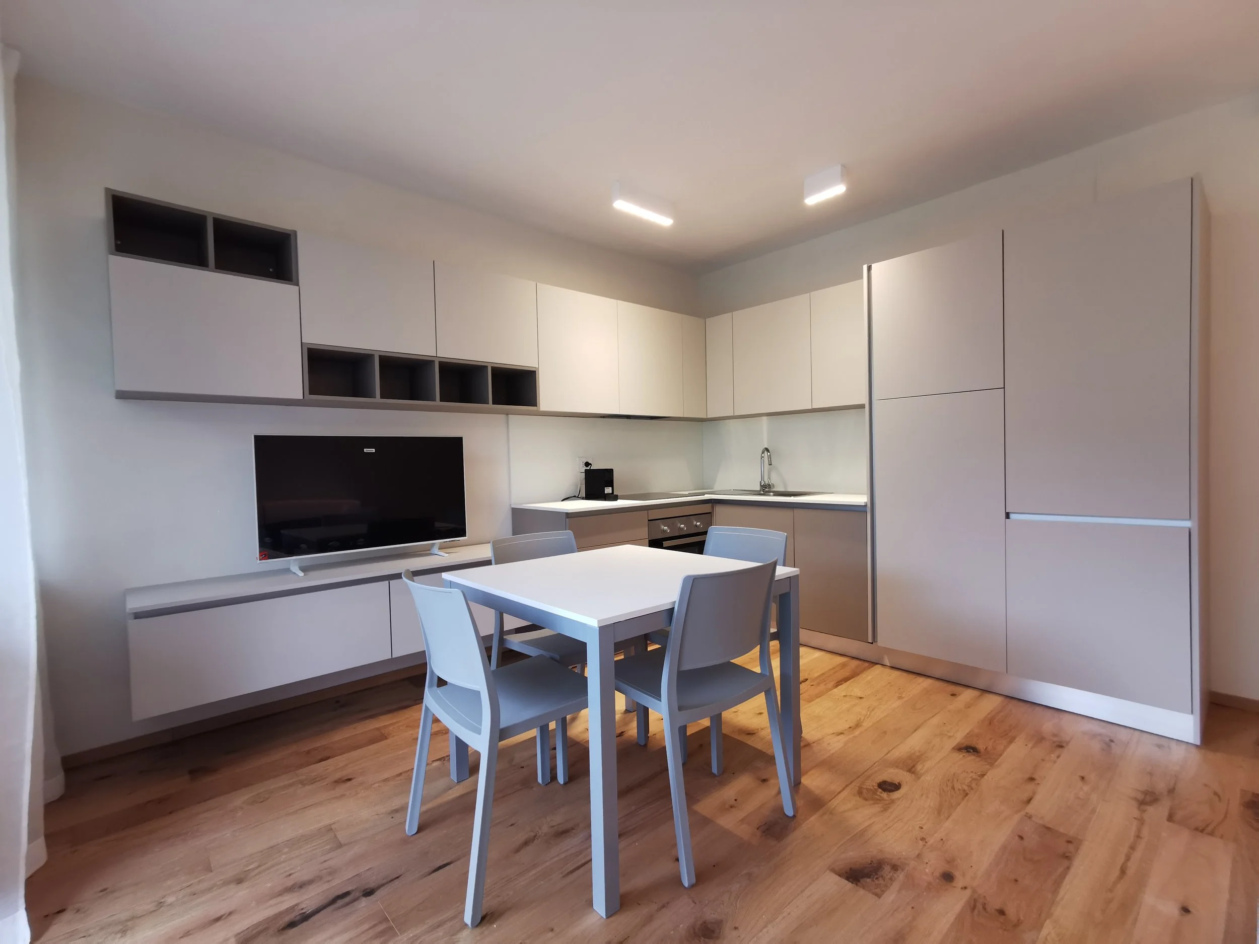 Cucina moderna con tavolo e sedie, armadietti chiari e televisore sospeso