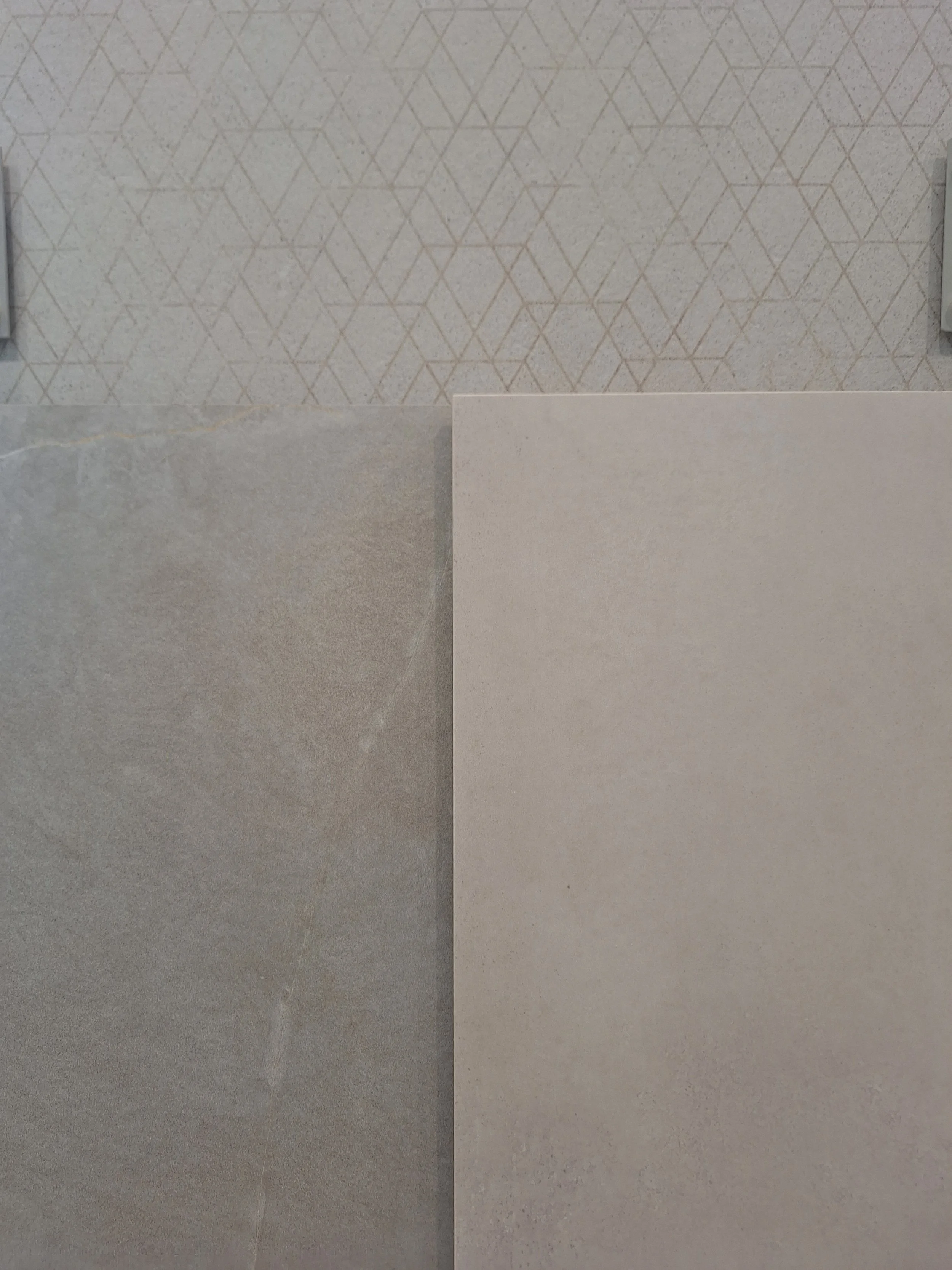 Tre campioni di piastrelle di diversi colori e texture, con una parete decorativa con un motivo geometrico in background.