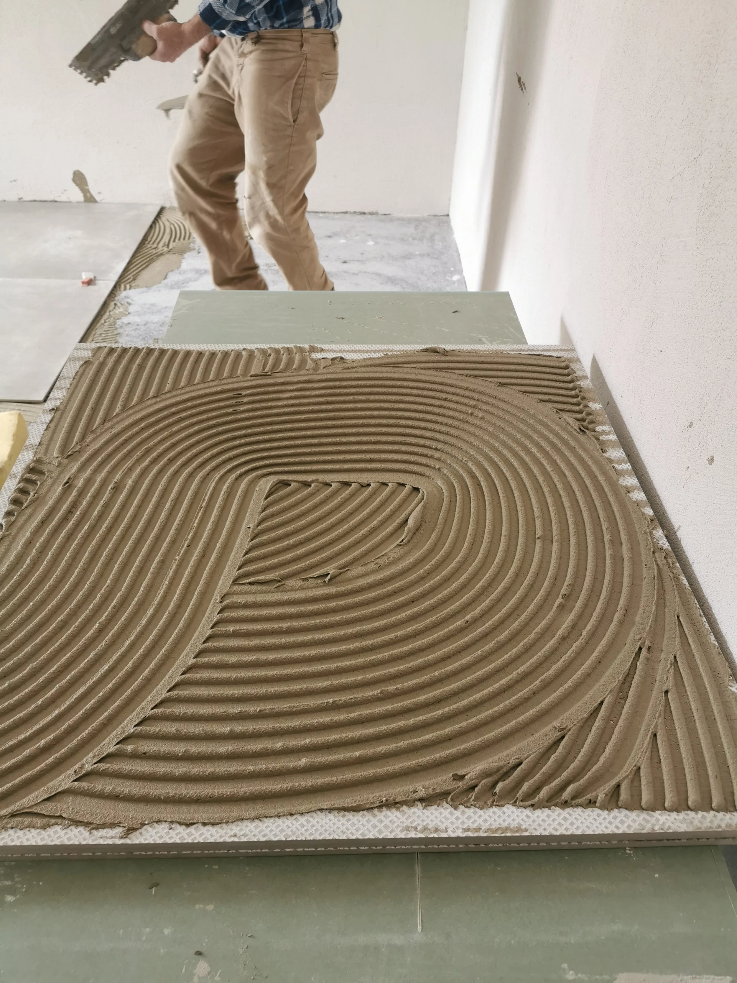 Mano che applica stucco o malta su una superficie di ceramica o piastrelle, in un ambiente di costruzione o ristrutturazione.