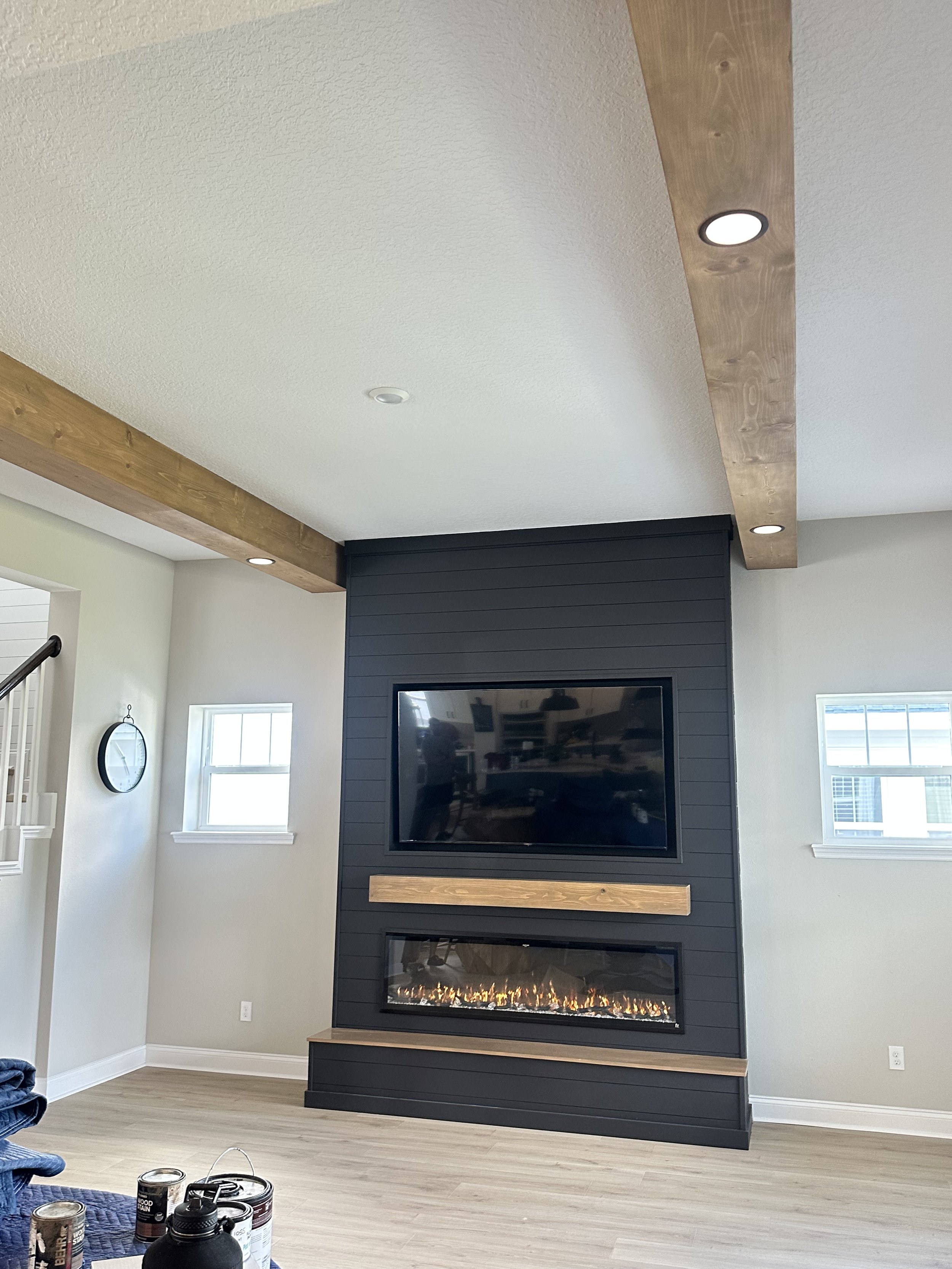Living room with black accent wall, mounted TV, electric fireplace, and wooden trim accents on ceiling and wall.