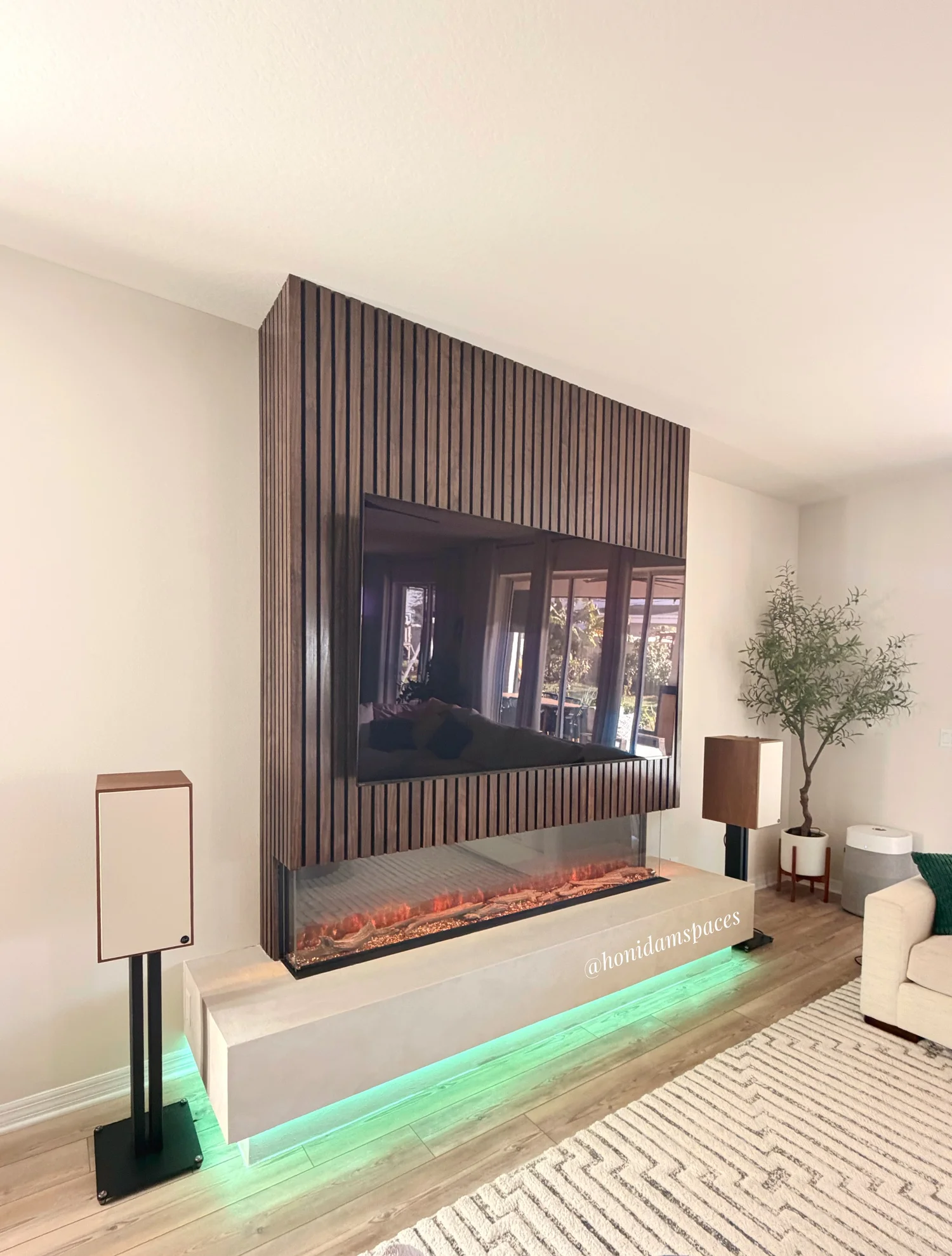 Modern living room with a built-in fireplace with green lighting, a wooden accent wall, and surrounding decor including lamps, a potted plant, and a sofa.
