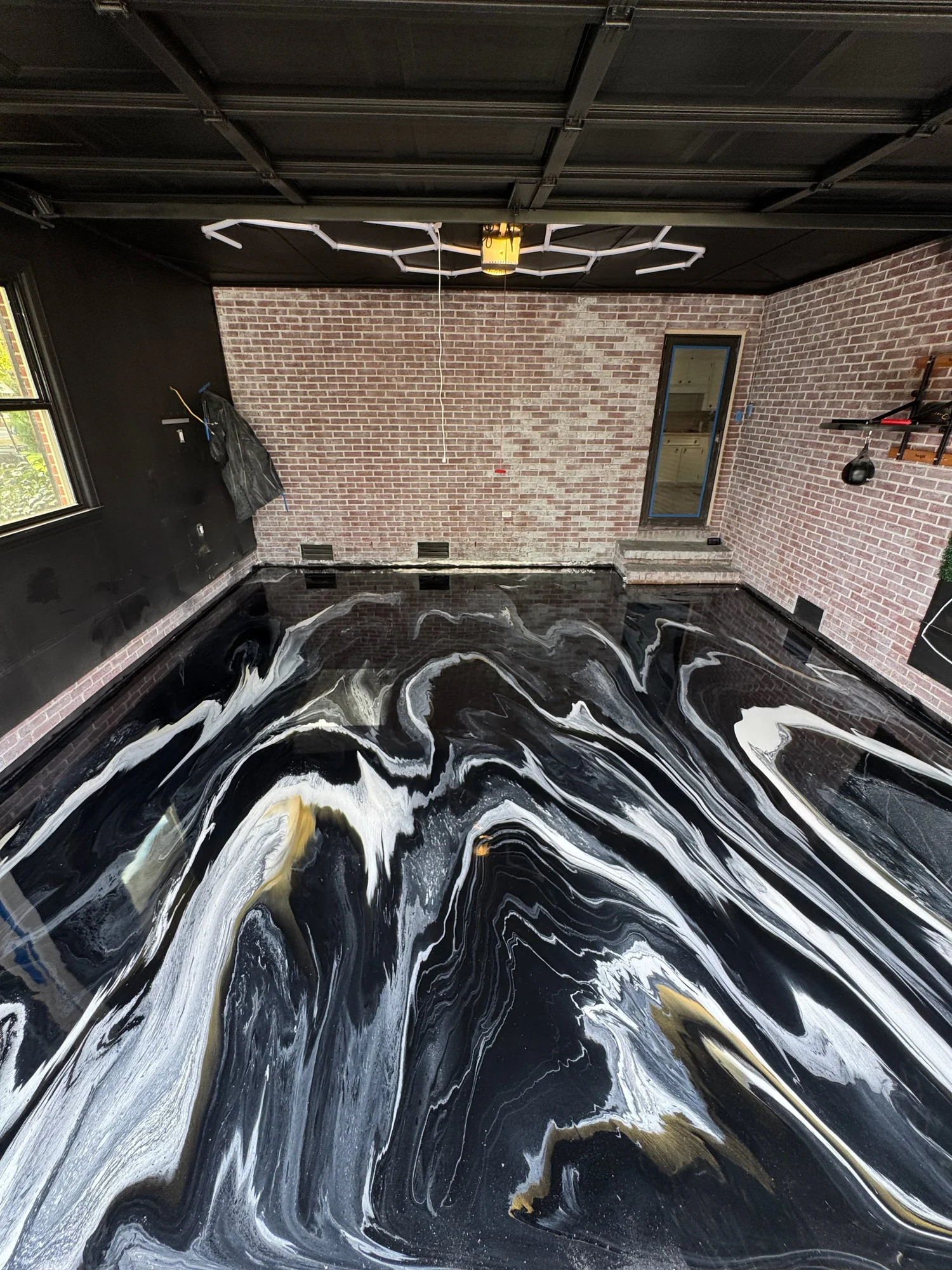 A room with exposed brick walls, a black ceiling with white geometric light fixtures, and a floor with a black, white, and gold marble swirl pattern. There is a window and a door on the walls.
